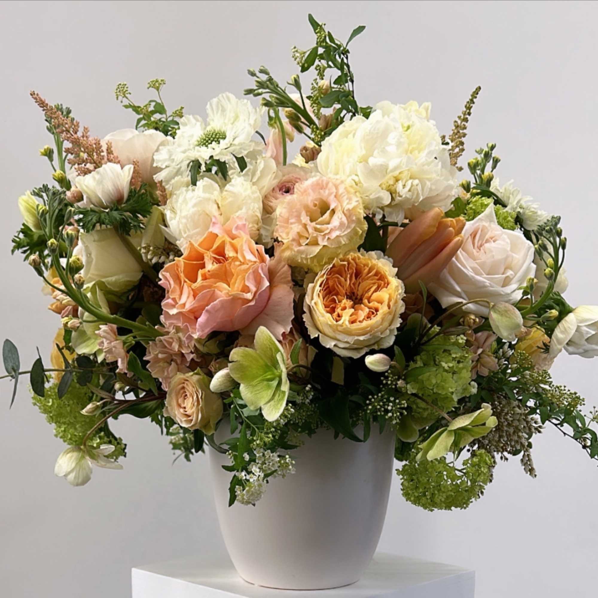 Mixed bouquet of peach, white, and green flowers in a white vase