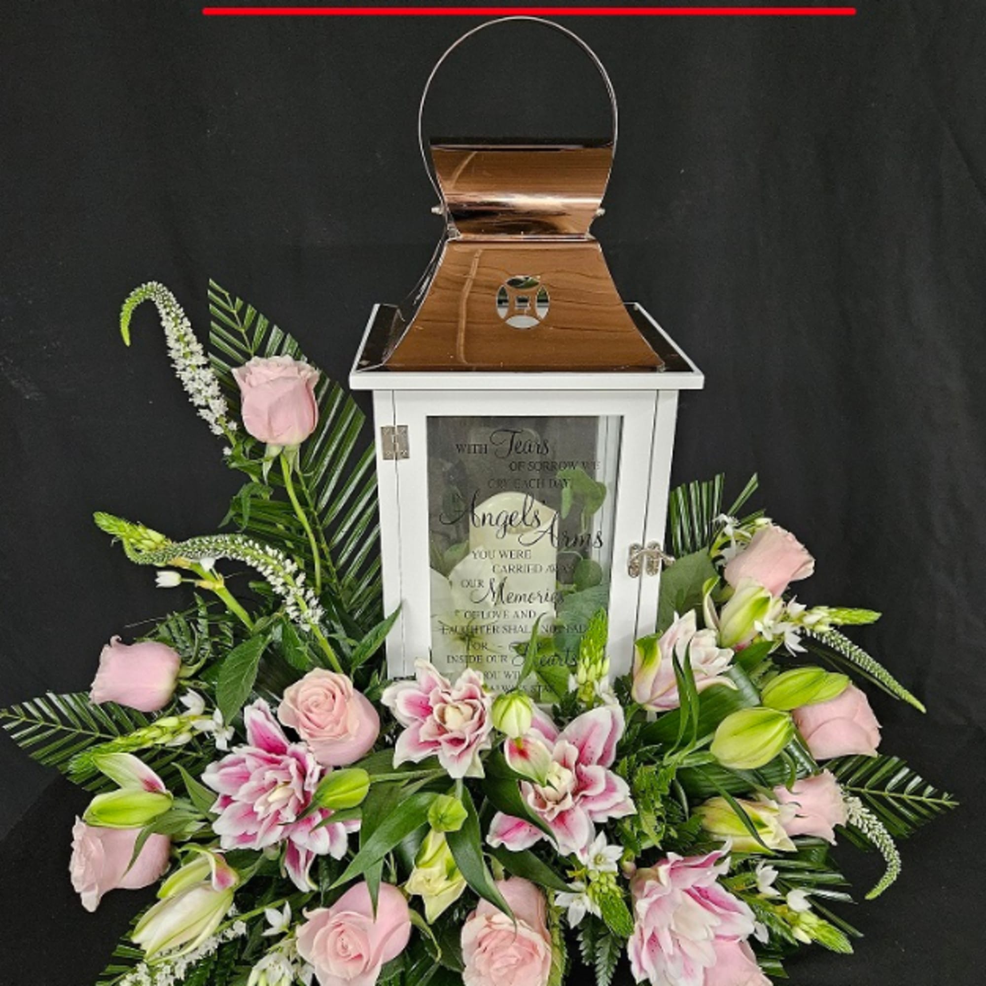 White memorial lantern surrounded by pink roses and lilies arranged in a low centerpiece
