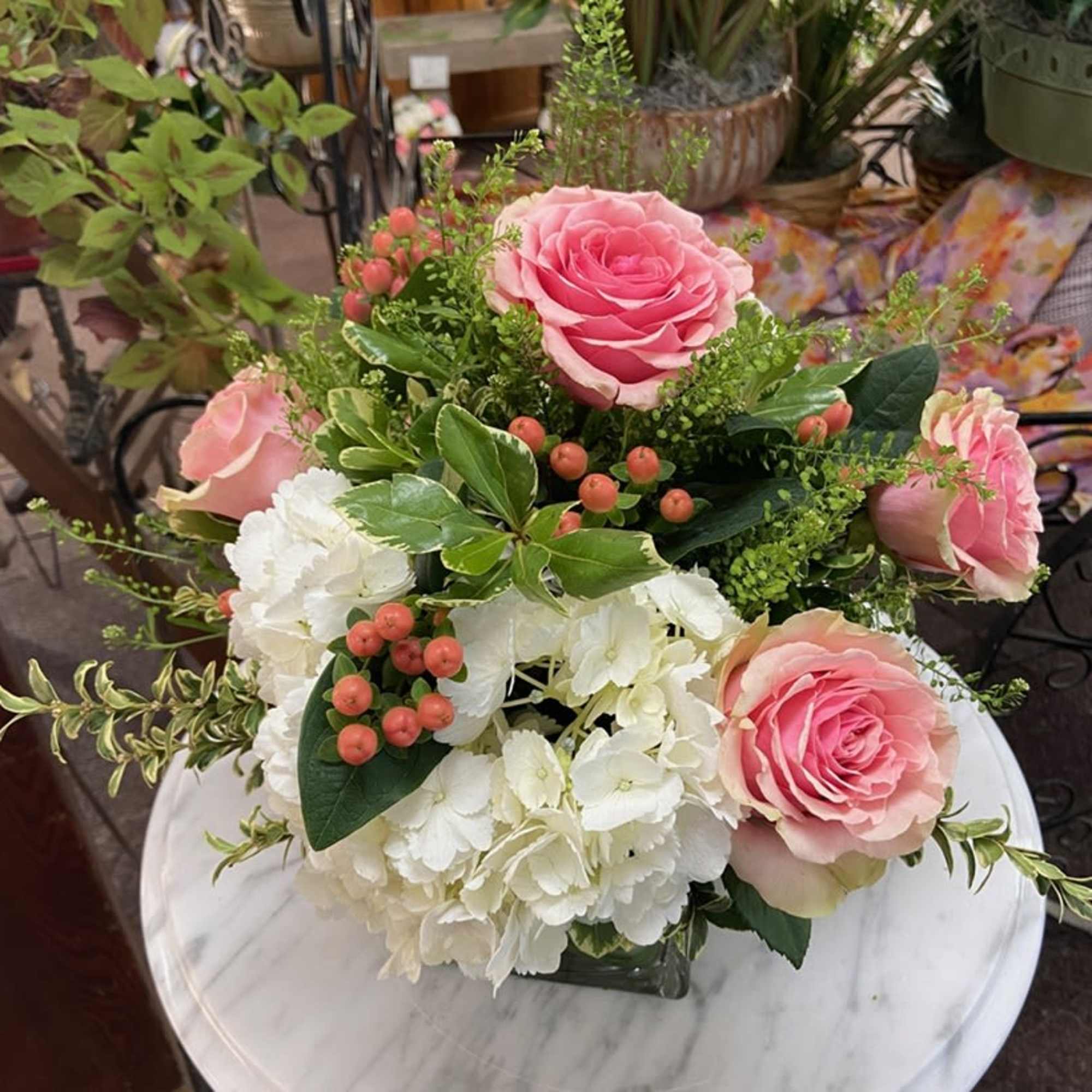 Pink roses and white hydrangeas with berries in a clear glass vase on a round marble table