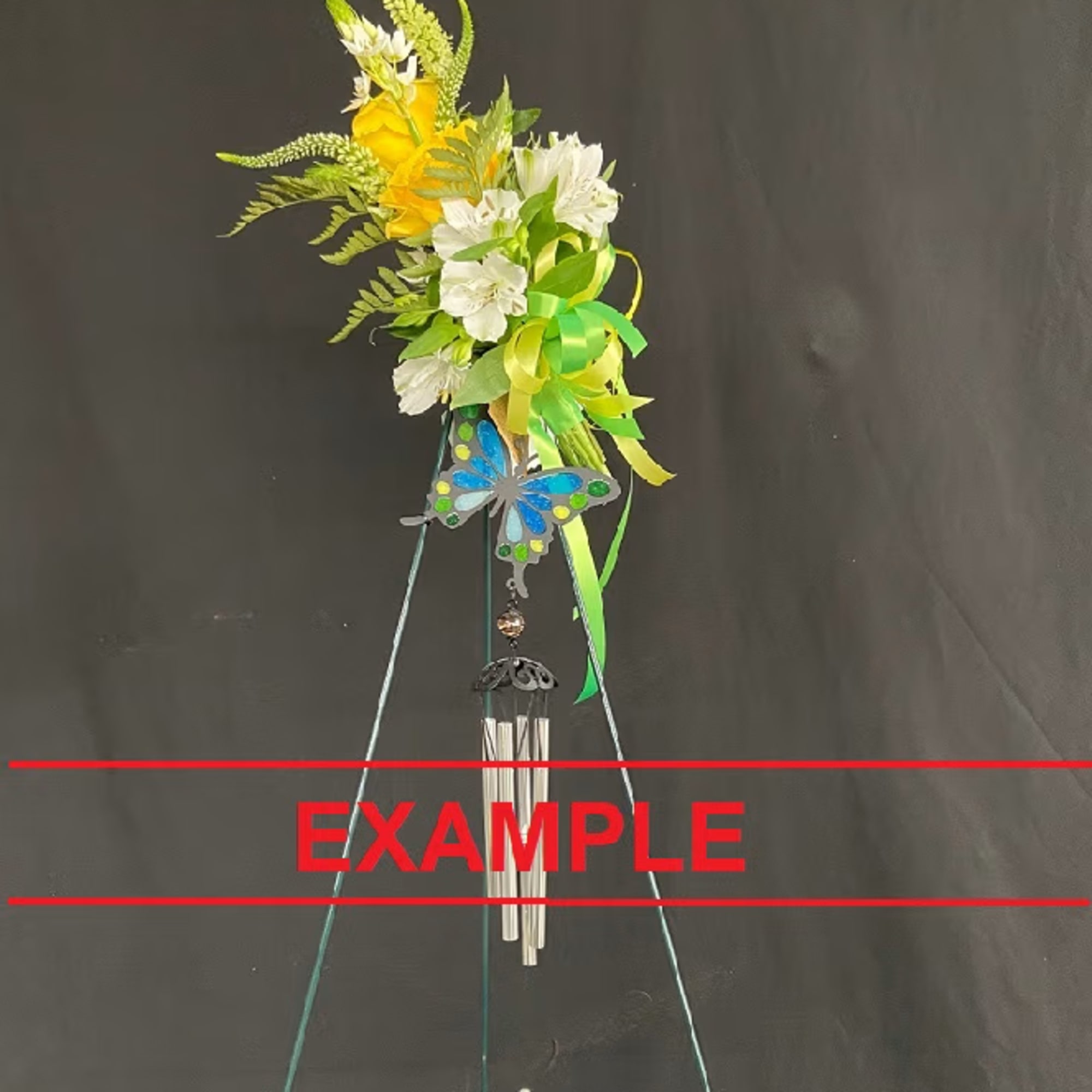 Tall green metal wind chime on a stand topped with yellow and white flowers, ribbon, and a blue butterfly decoration