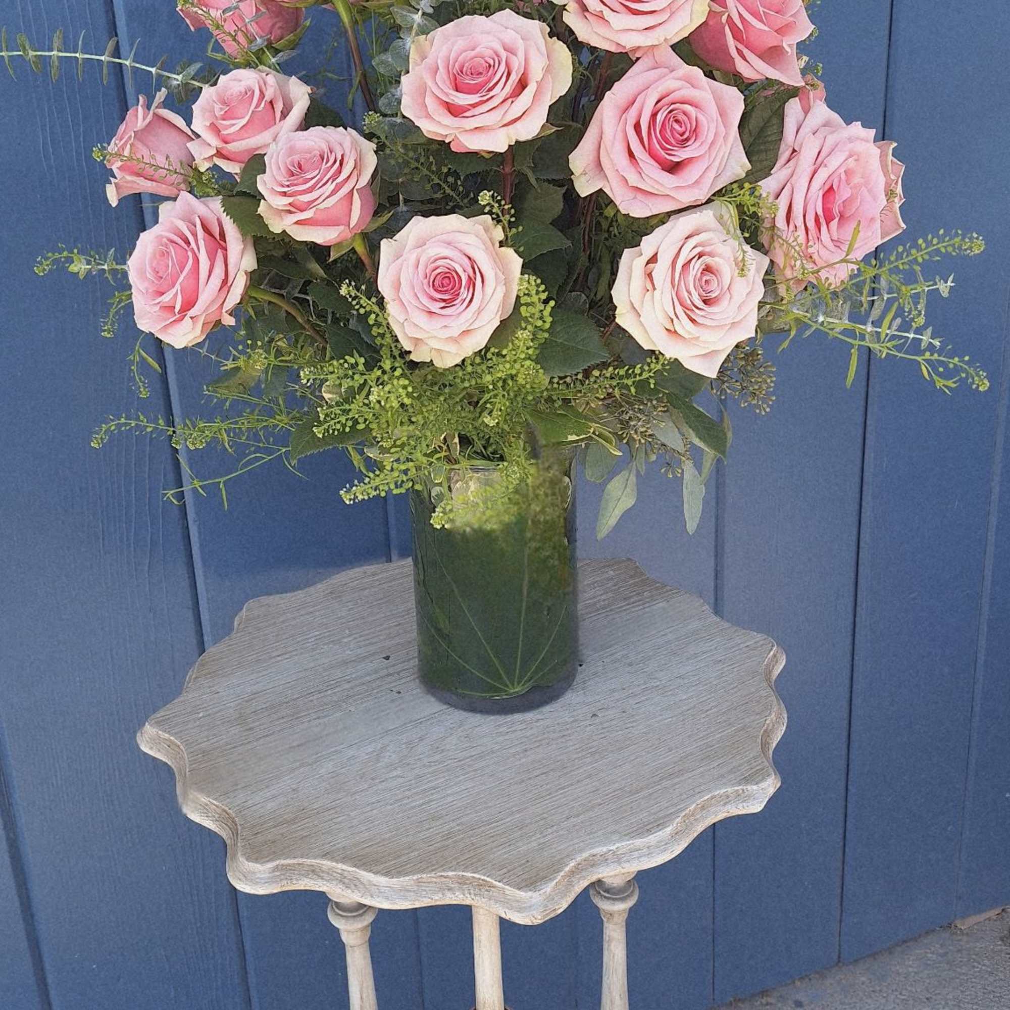 Large arrangement of pink roses in a clear glass vase on a small wooden table