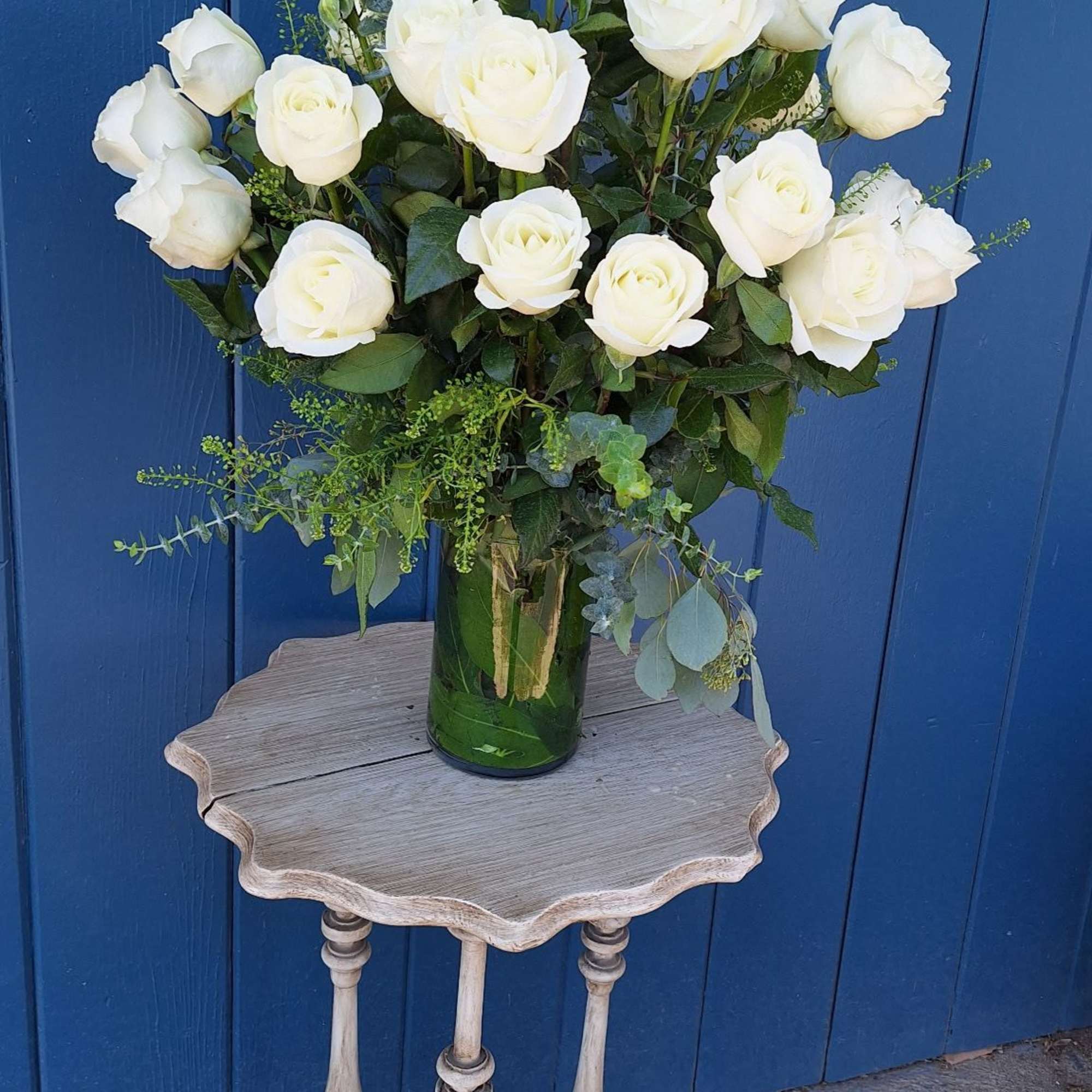 Tall arrangement of white roses in a clear glass vase on a small wooden table