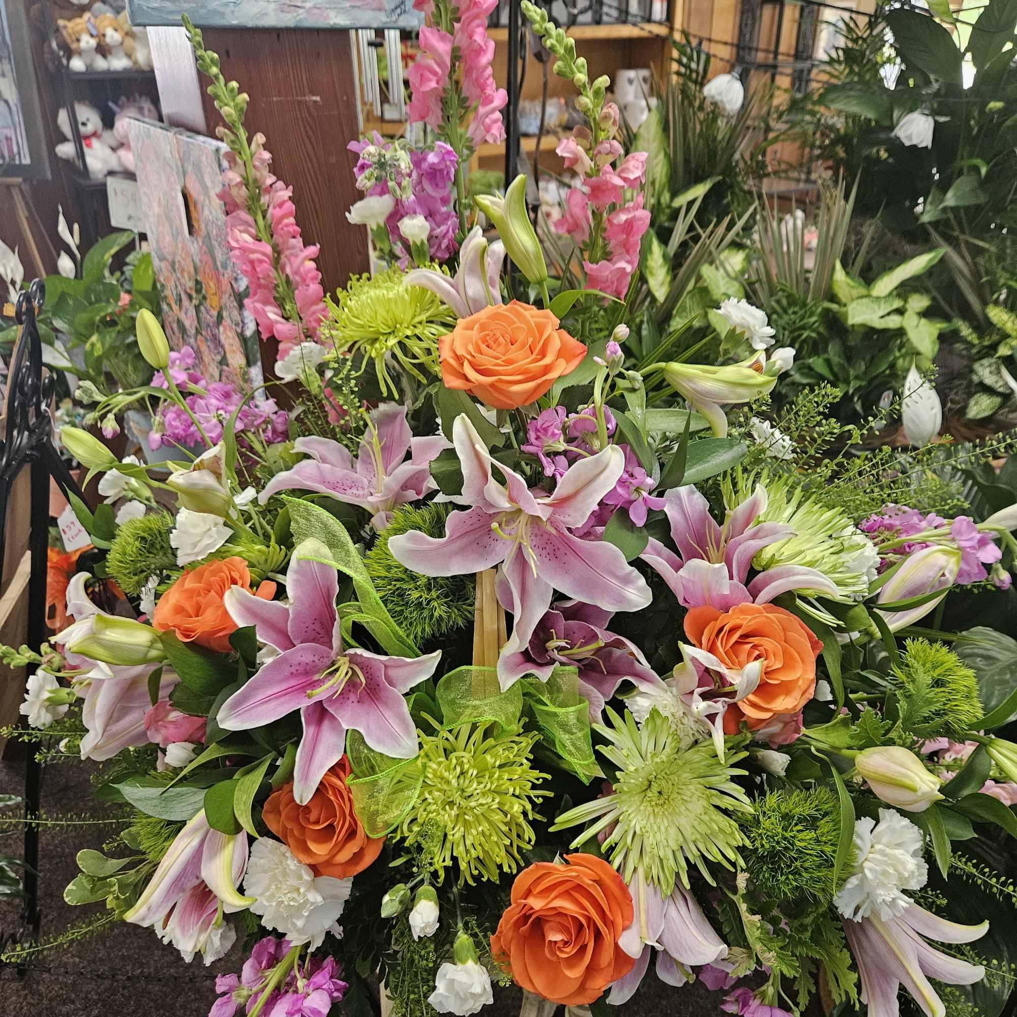 Tall arrangement of pink lilies, orange roses, green mums, and pink snapdragons on a stand