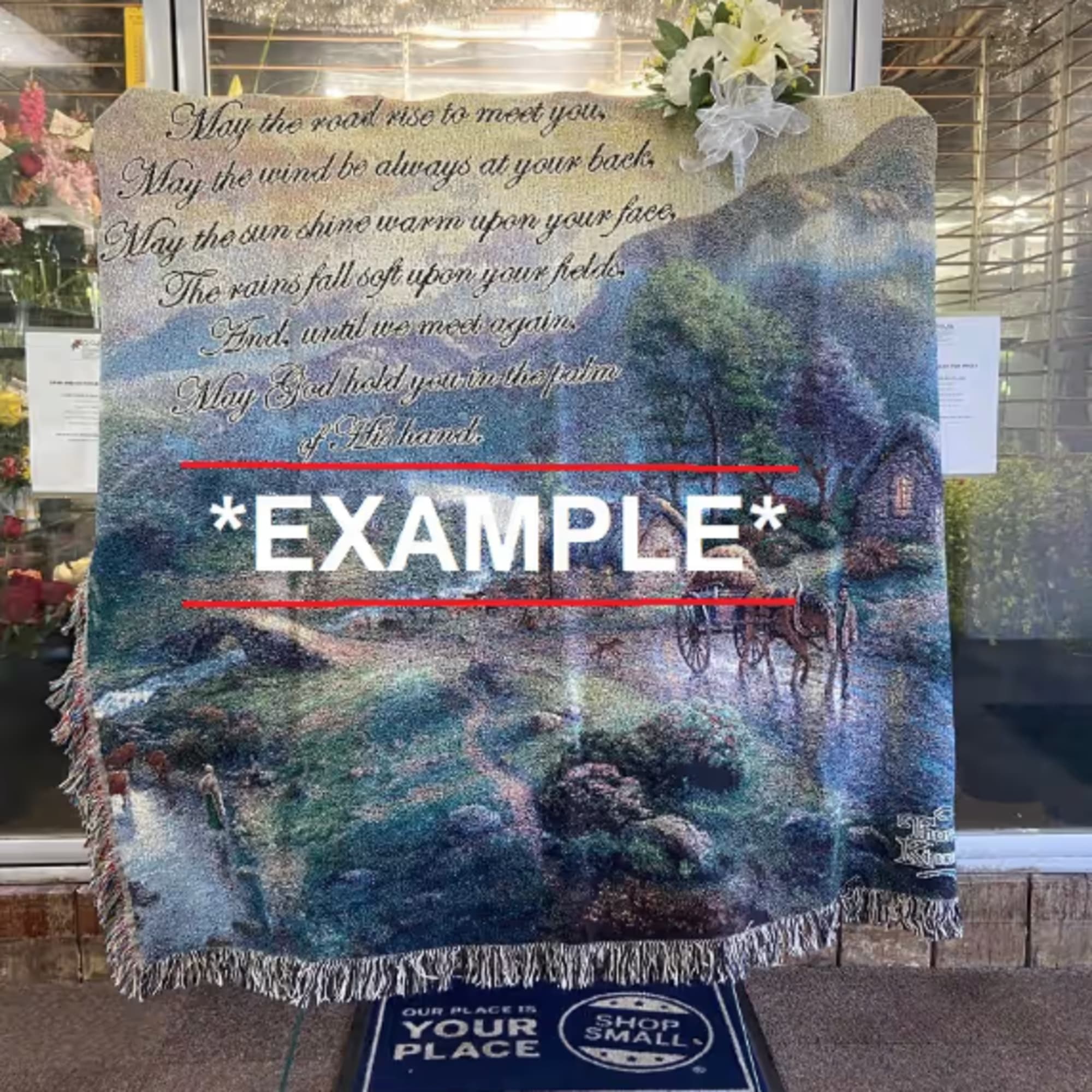Woven memorial blanket with Irish blessing text and small white lily spray at the top corner.