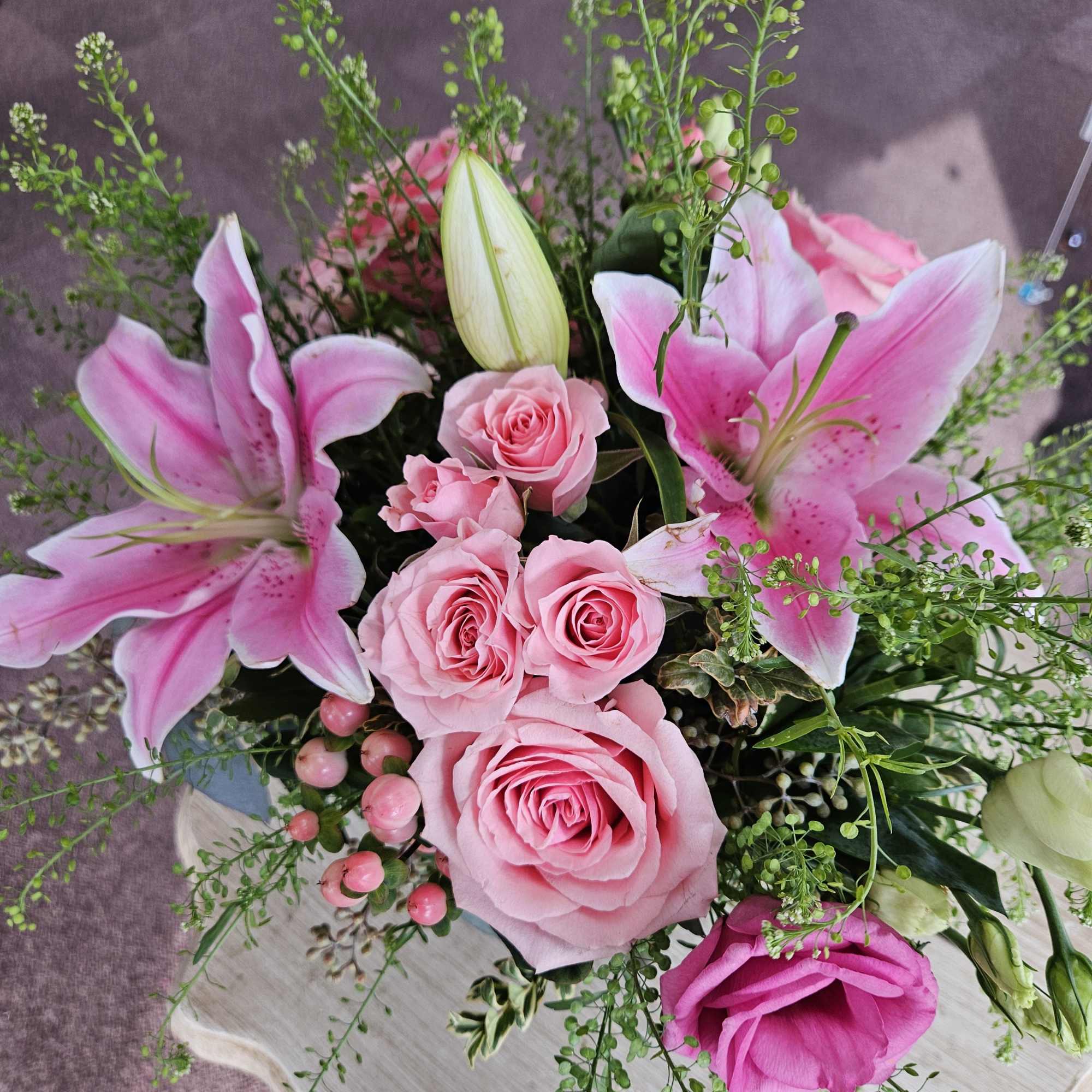 Pink roses and lilies with lisianthus and berries arranged in a lush mixed bouquet.