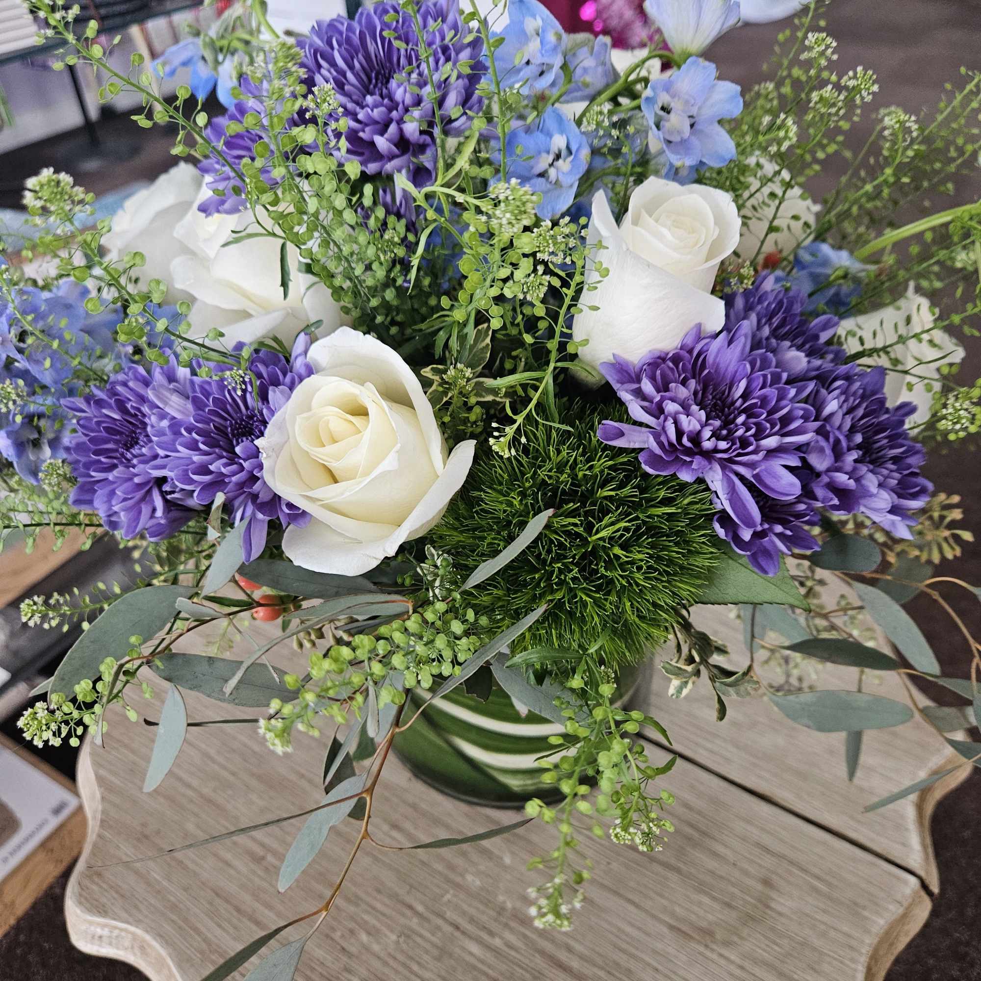 Arrangement of white roses, purple mums, and blue flowers in a clear glass vase