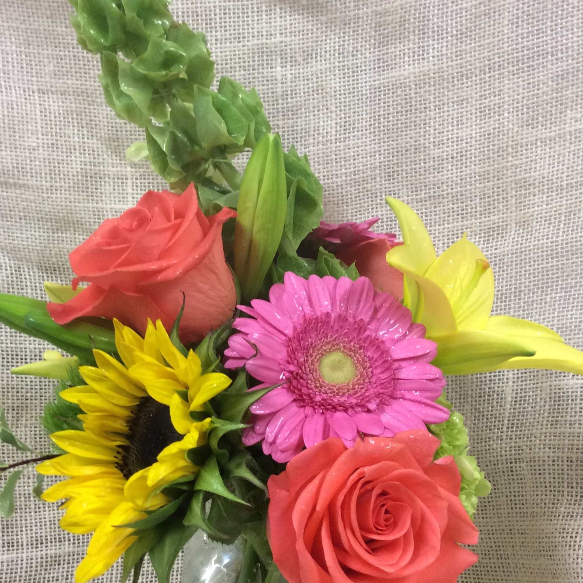 Bouquet of roses, gerbera daisies, sunflowers, and lilies in a glass vase