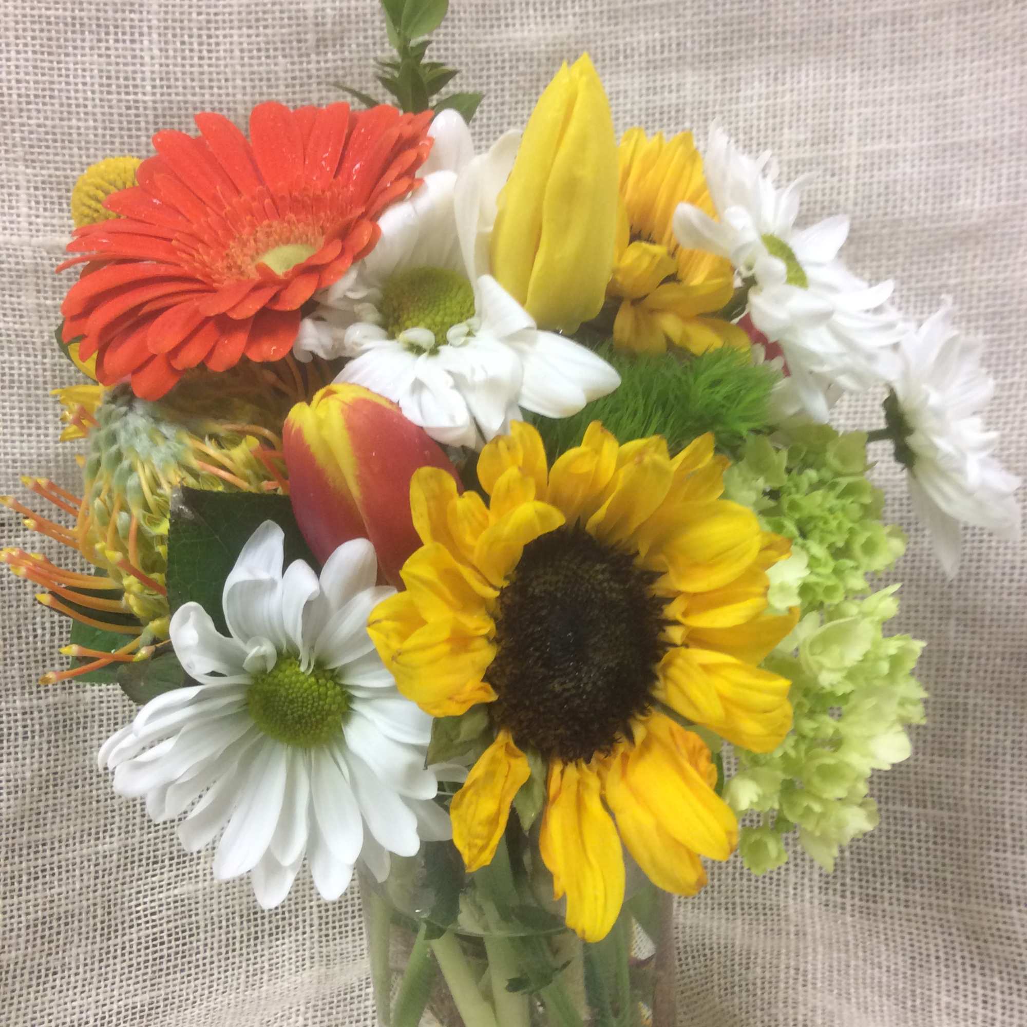Mixed bouquet of sunflowers, daisies, and gerbera daisies in a glass vase