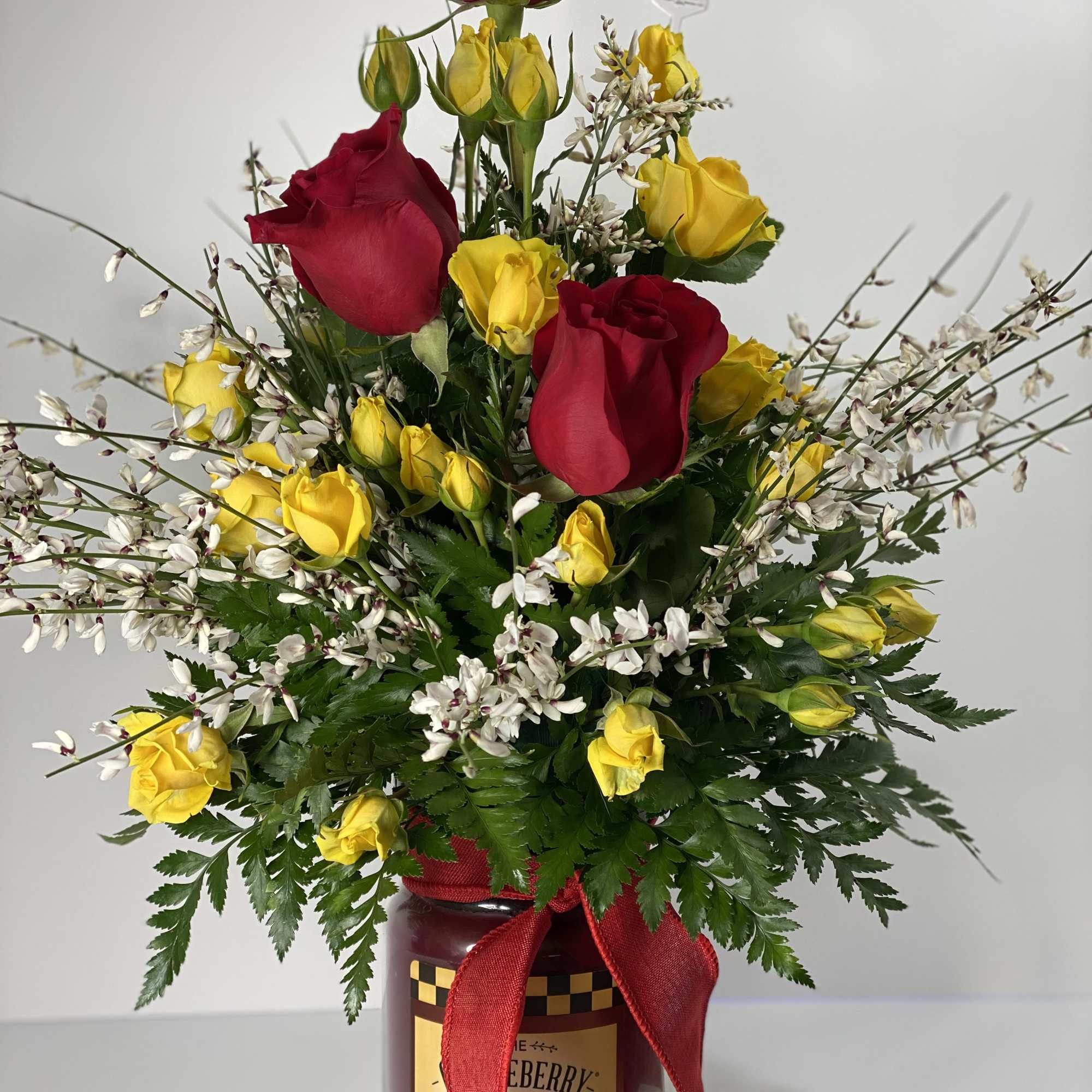 Red and yellow roses in a glass jar with a red ribbon
