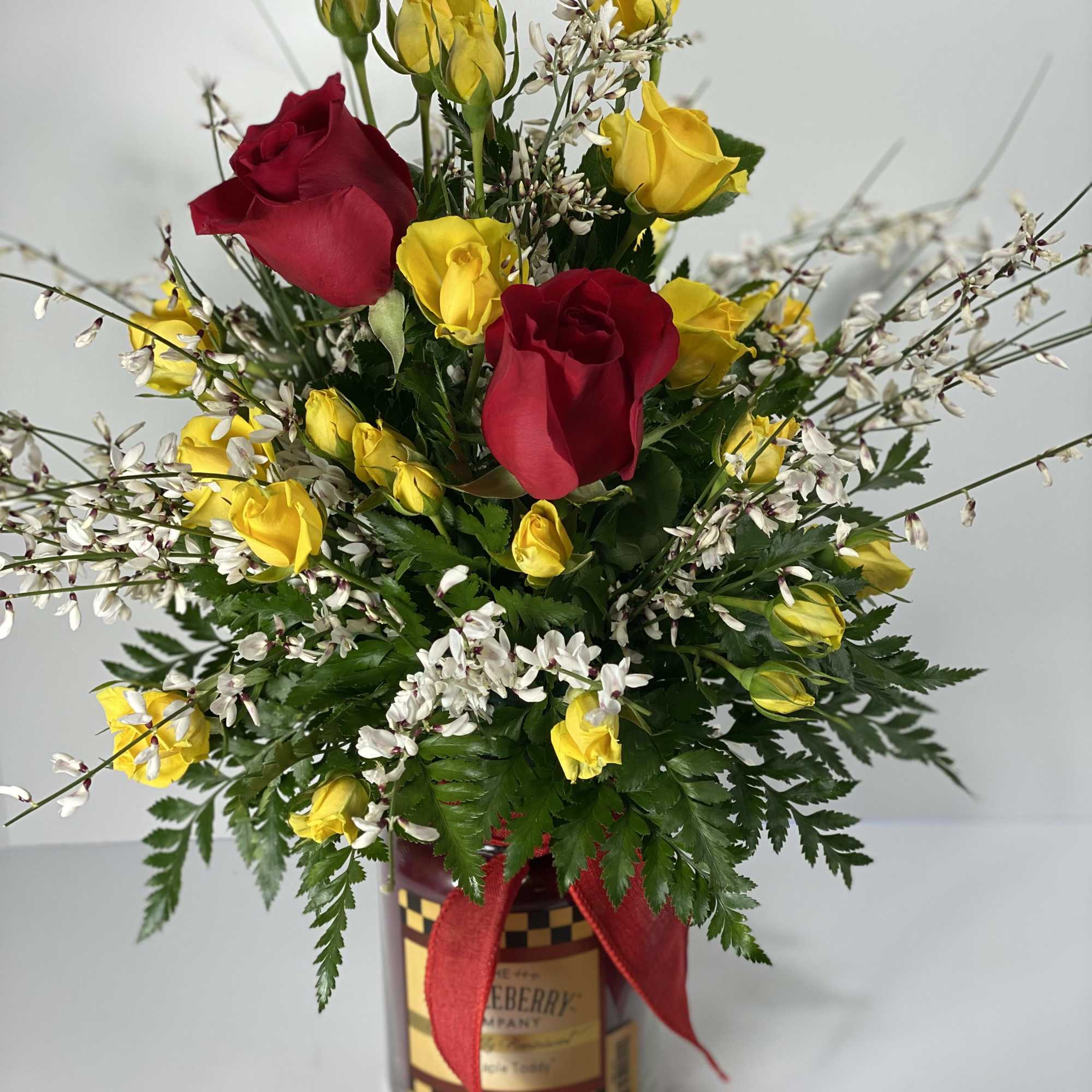 Red and yellow roses arranged in a glass jar with a red ribbon.