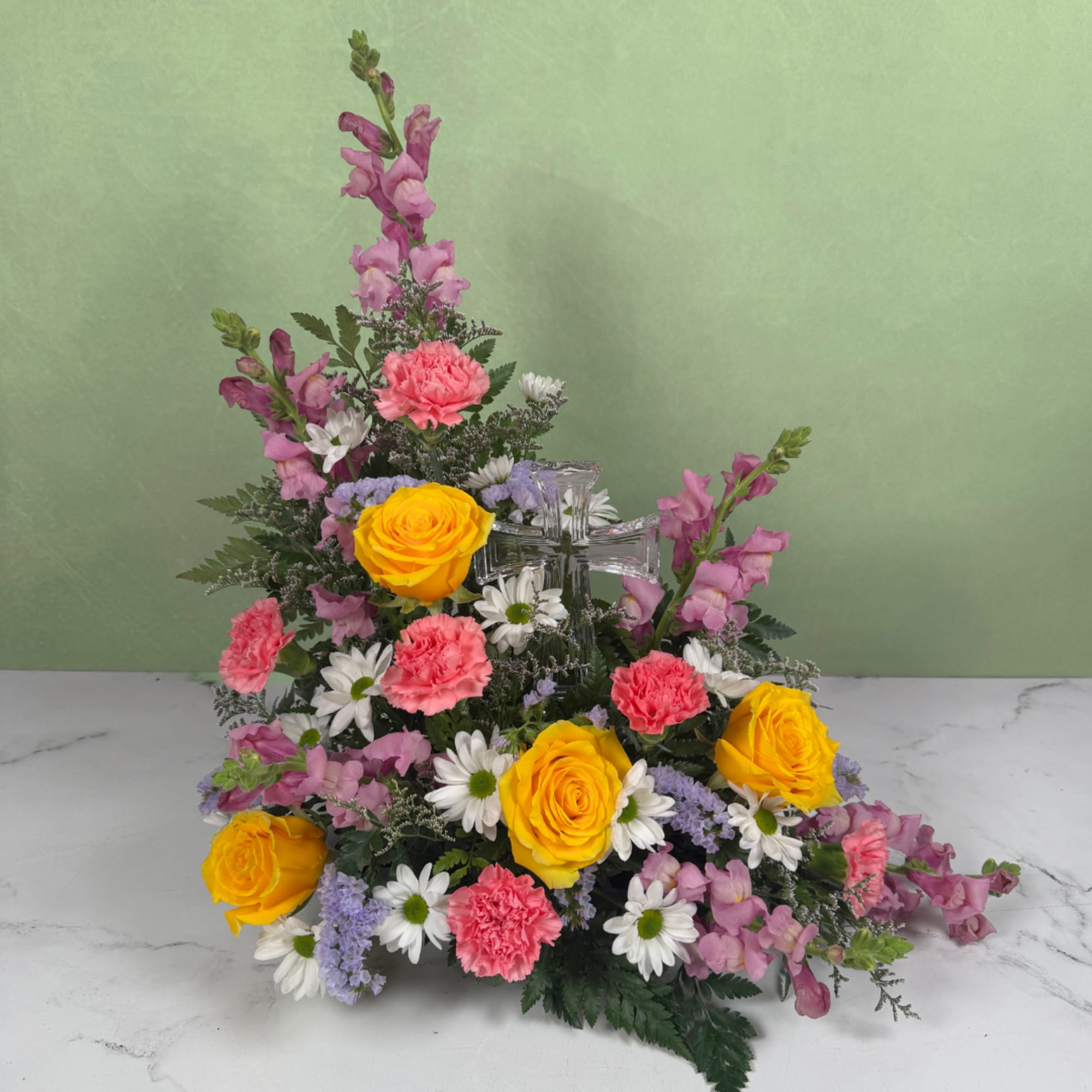 A clear glass cross nestled at the heart of softly layered blooms, photo 2 of 3