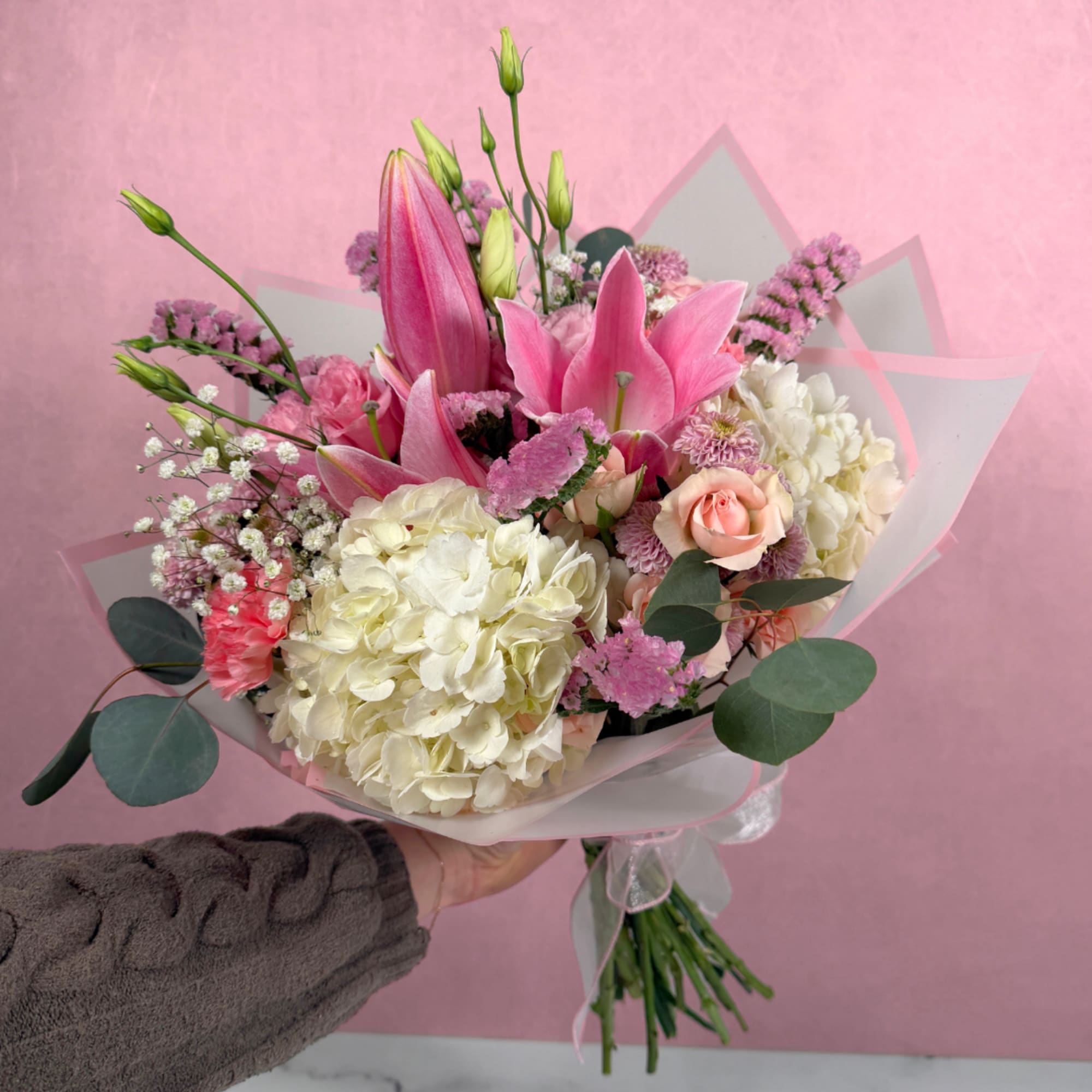 Pink lilies and hydrangeas in a wrapped bouquet with roses