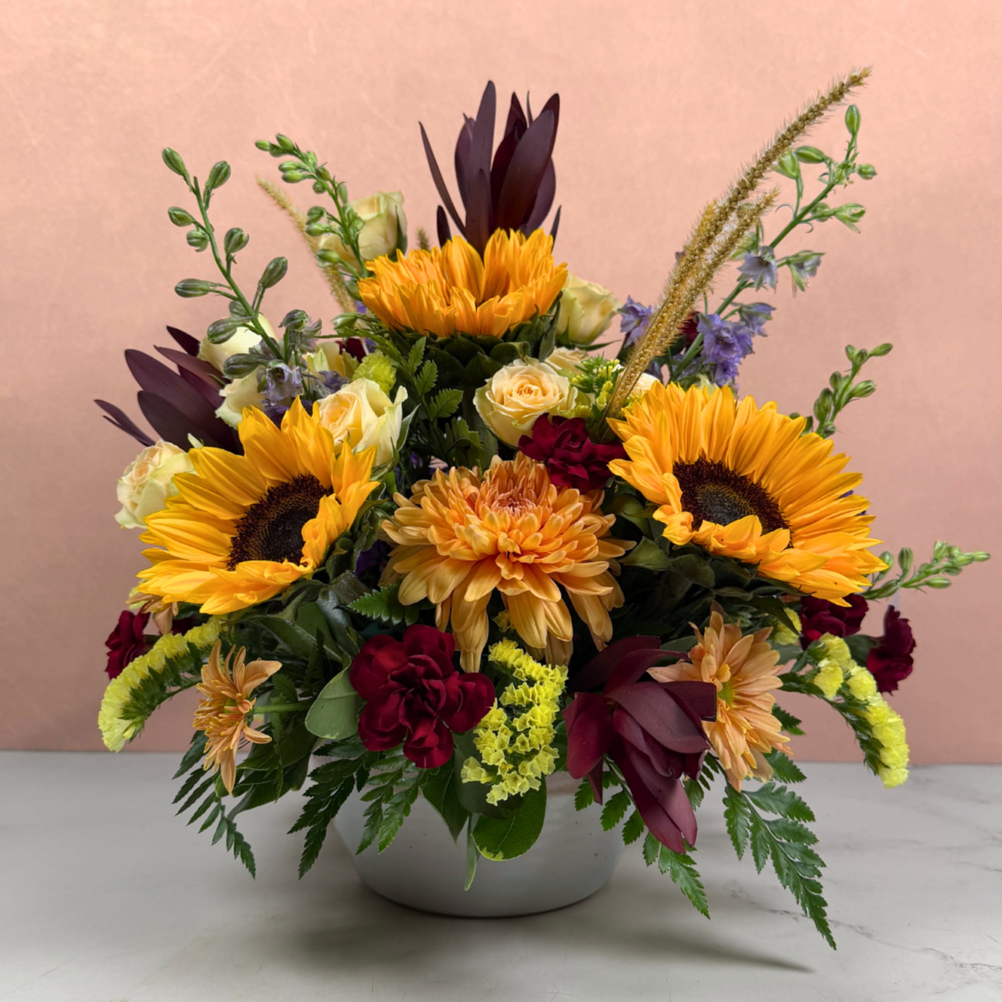 Mixed bouquet with sunflowers, roses, and chrysanthemums in a white bowl vase