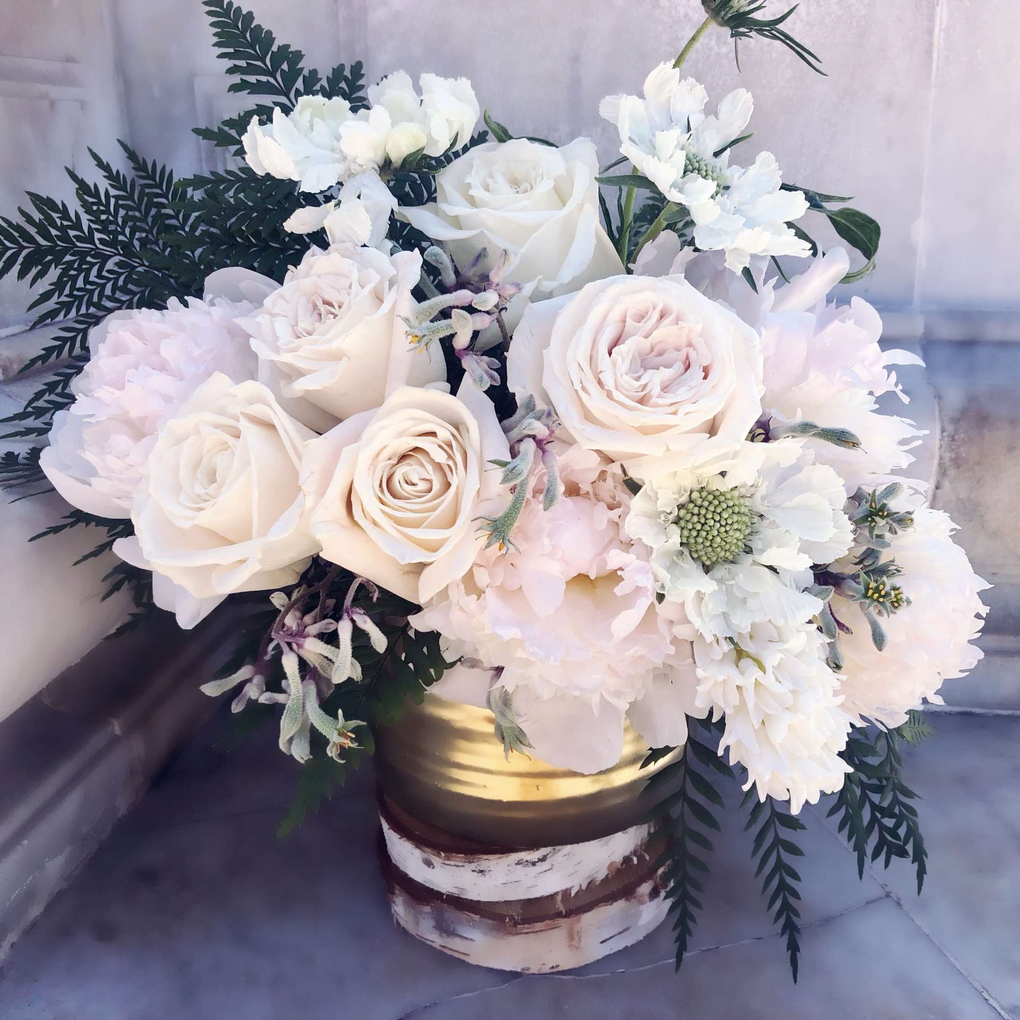 White and ivory roses with soft white blooms in a gold and white cylinder vase