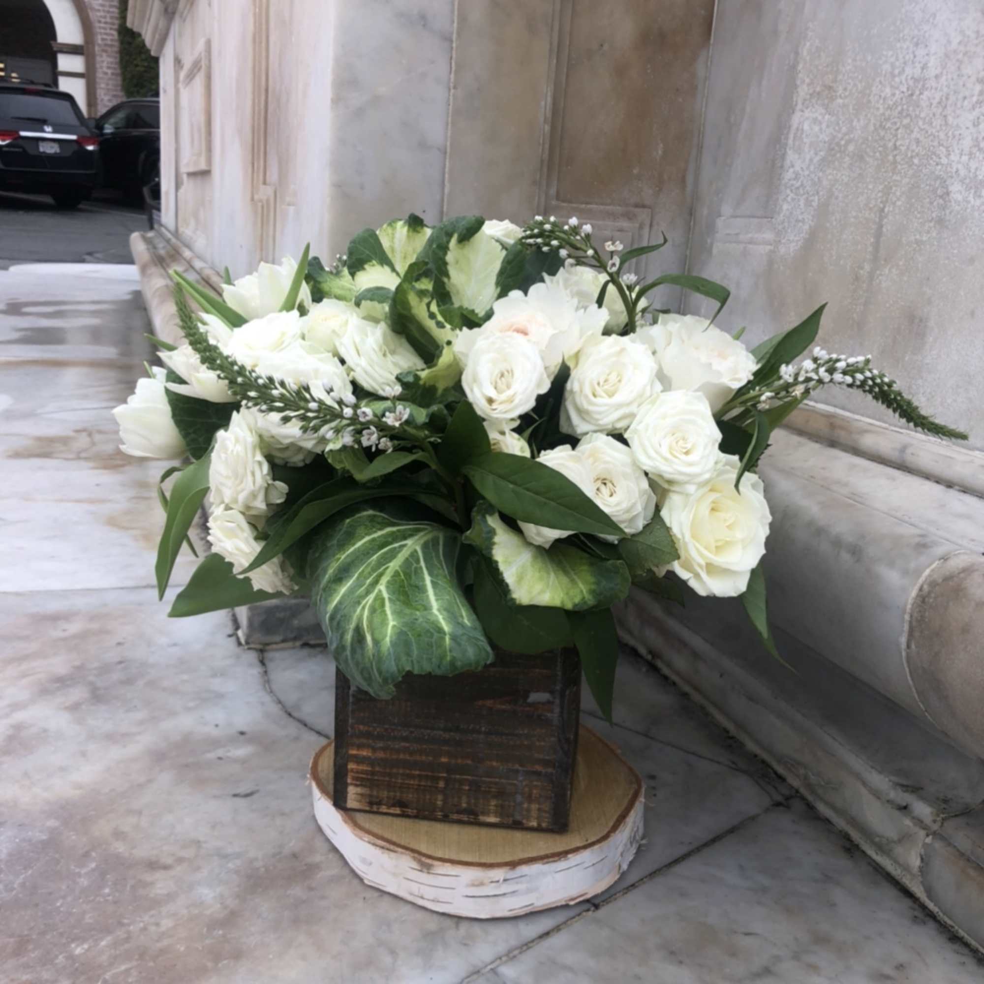 White rose arrangement in a wooden box with green foliage