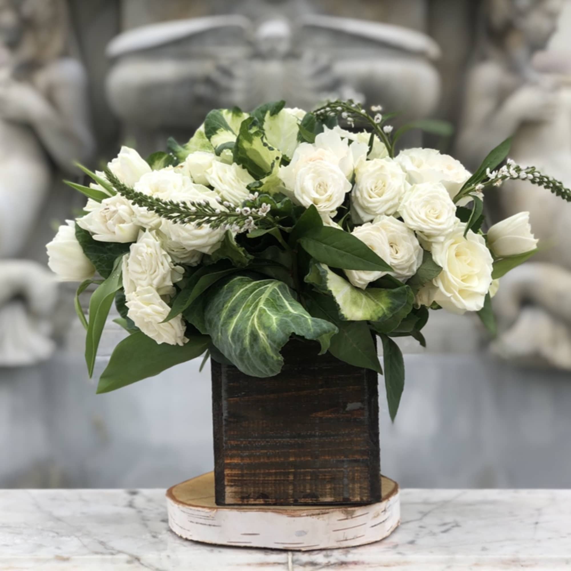 White rose arrangement in a dark wooden box on a round base