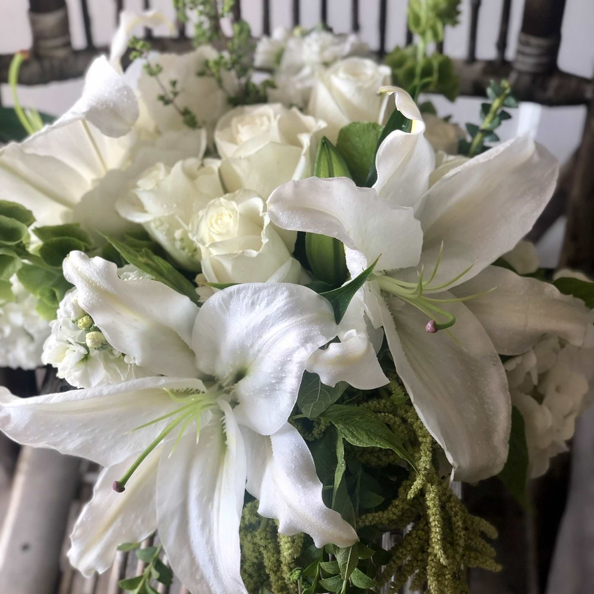 All-white arrangement of lilies, roses, and hydrangeas with cascading green accents