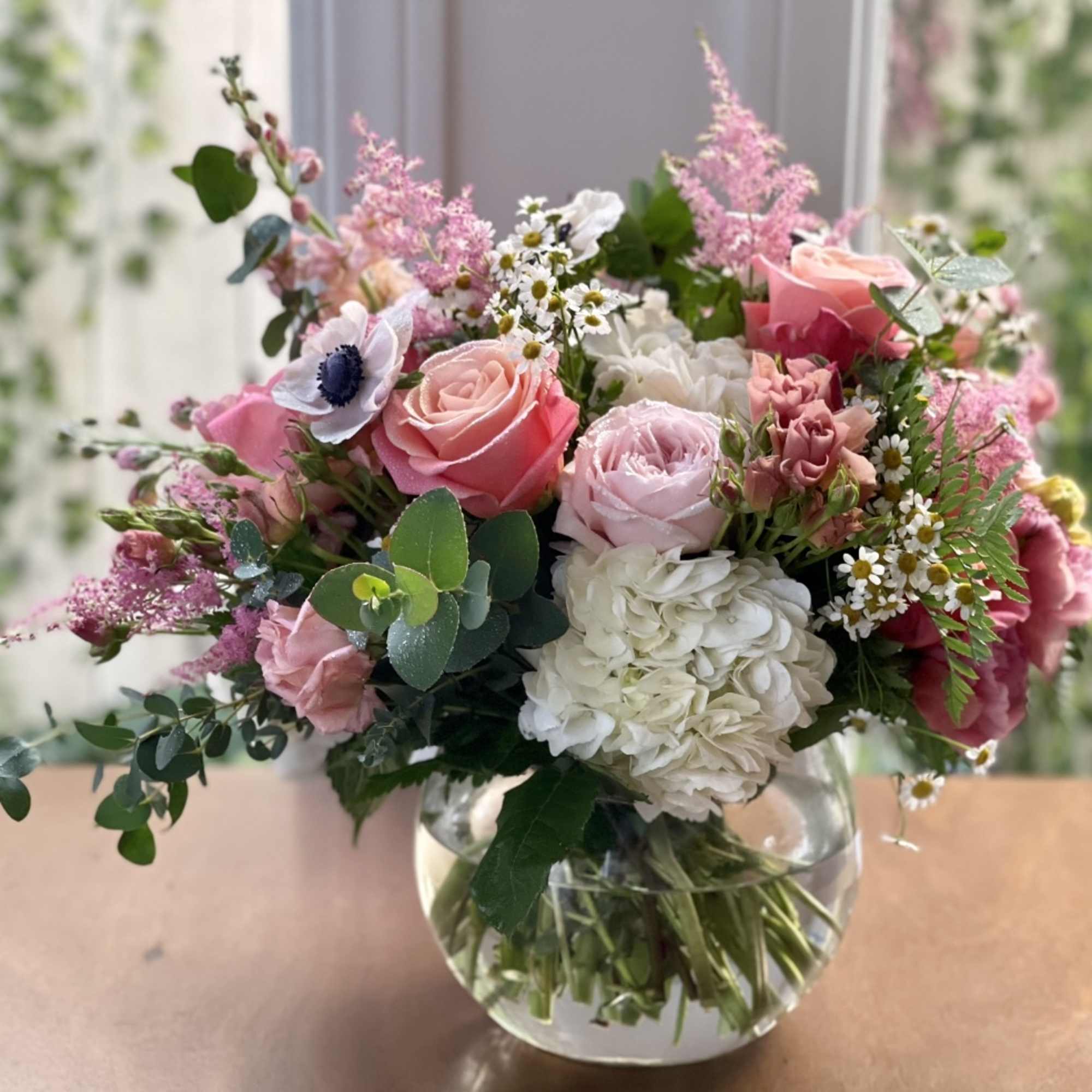 Round glass vase with pink roses, white hydrangeas, anemones, and small white daisies.
