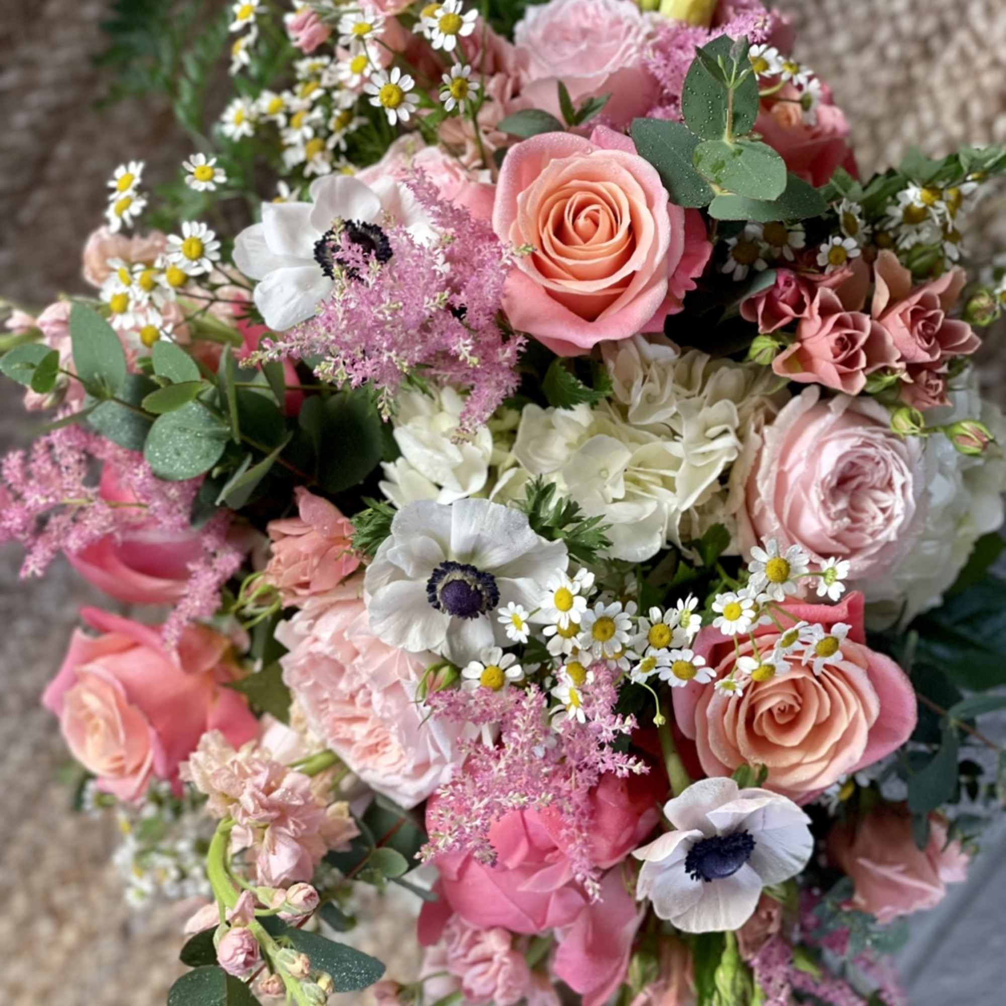 Hand-tied bouquet of pink roses, white anemones, daisies, and mixed pastel flowers in a lush, rounded design