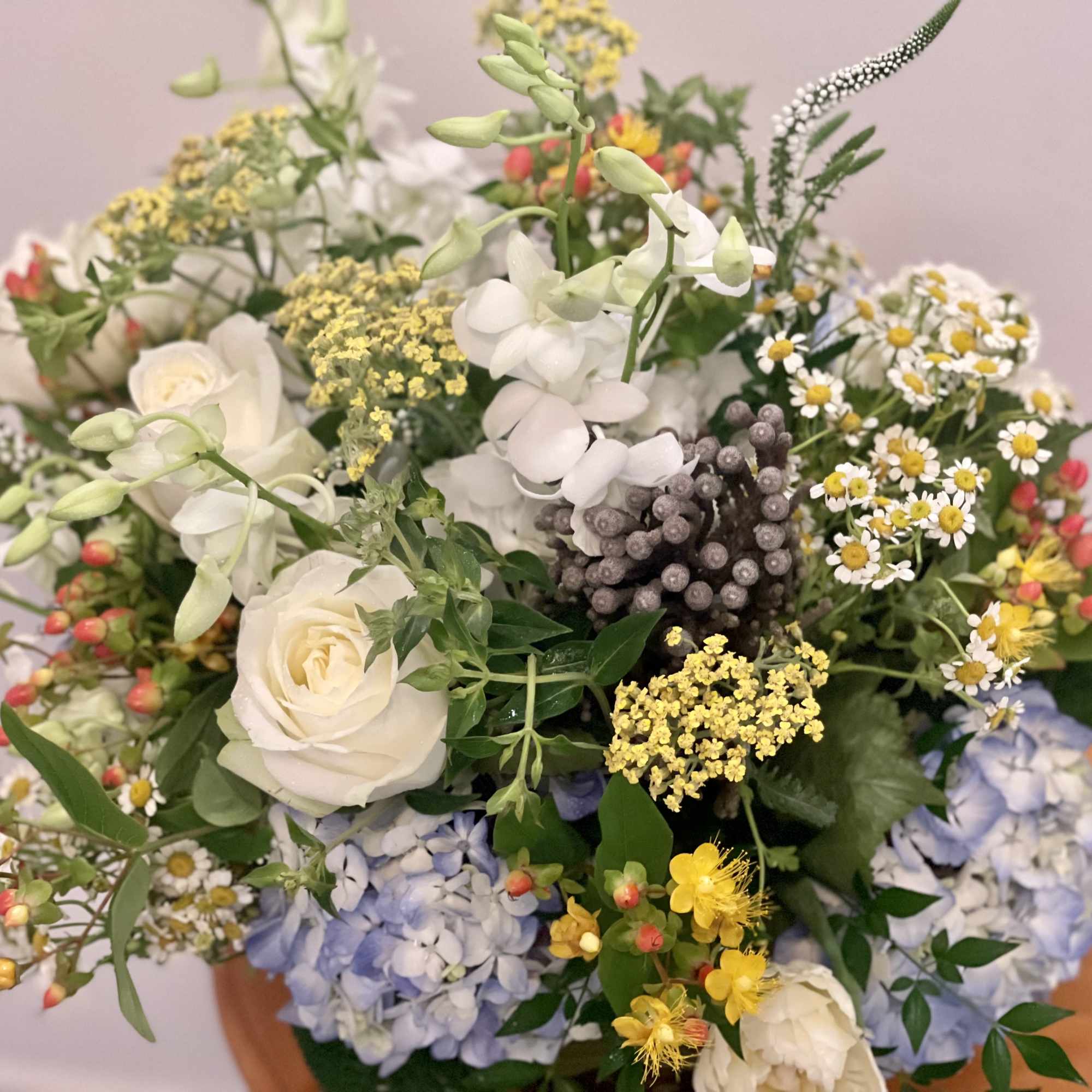 Mixed arrangement of white roses, blue hydrangeas, and small yellow and white blooms