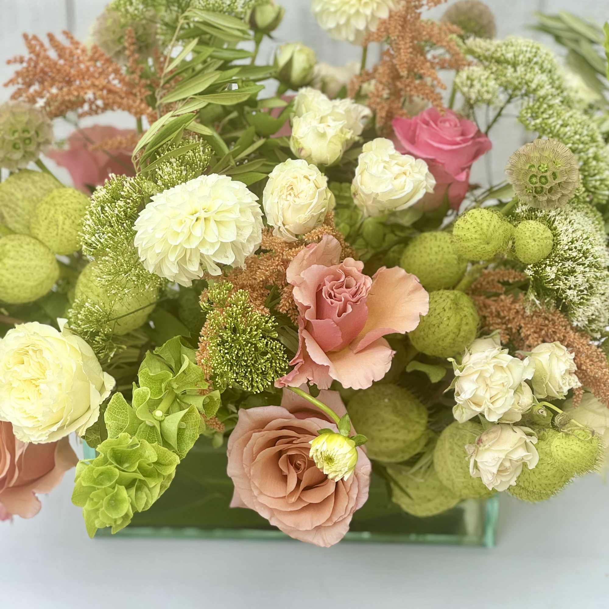Mixed bouquet of blush, white, and green flowers in a glass vase
