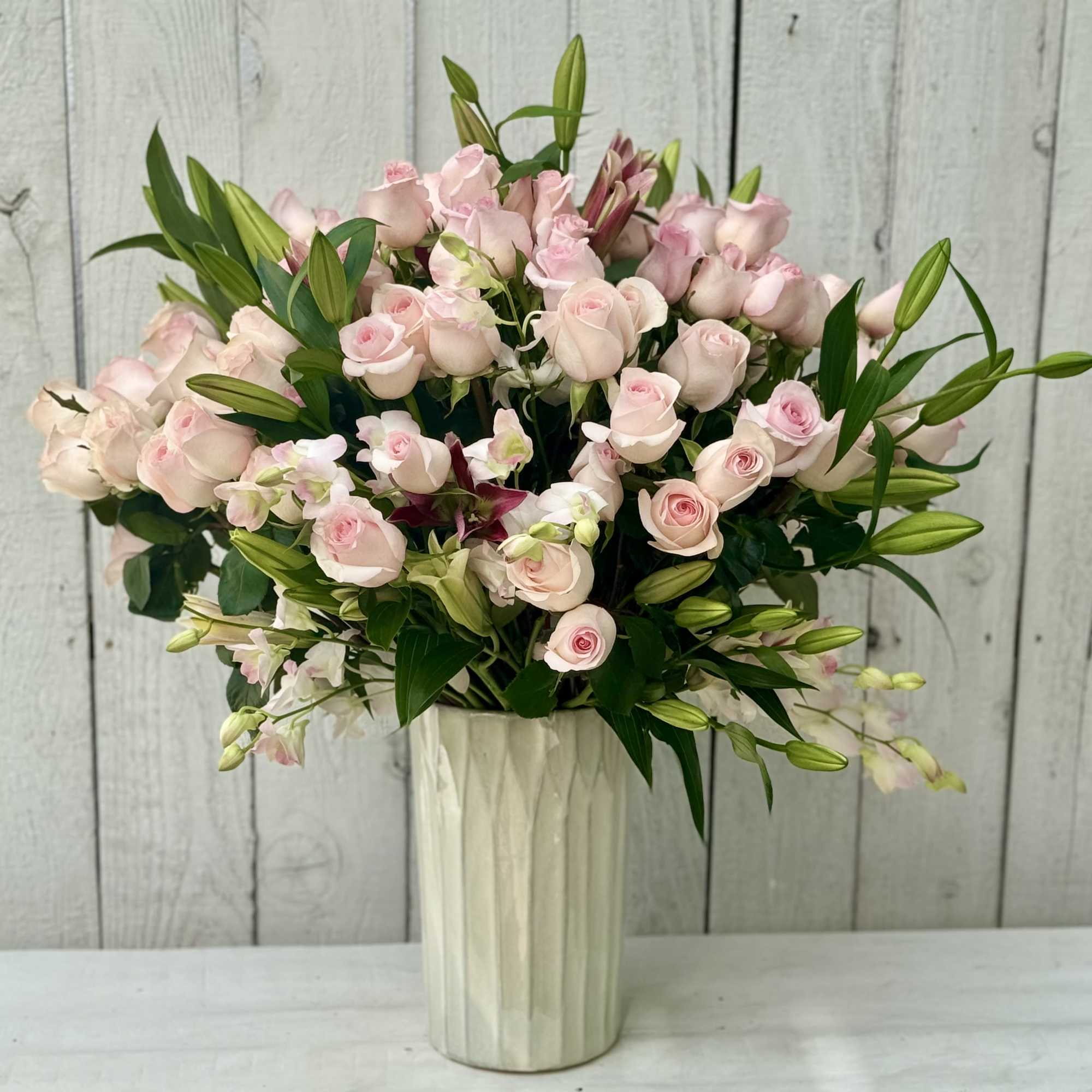Pink roses and lilies arranged in a tall white vase