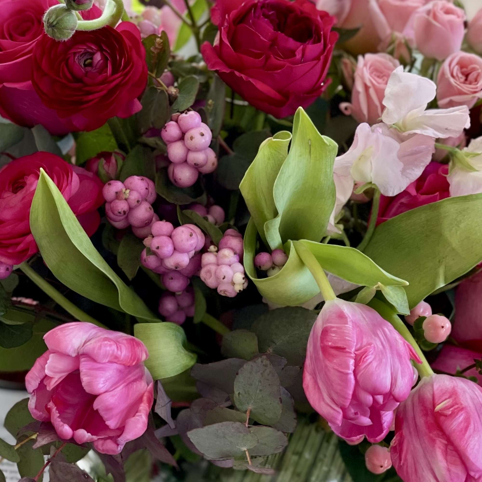 Arrangement of pink roses, tulips, and ranunculus in a round glass vase