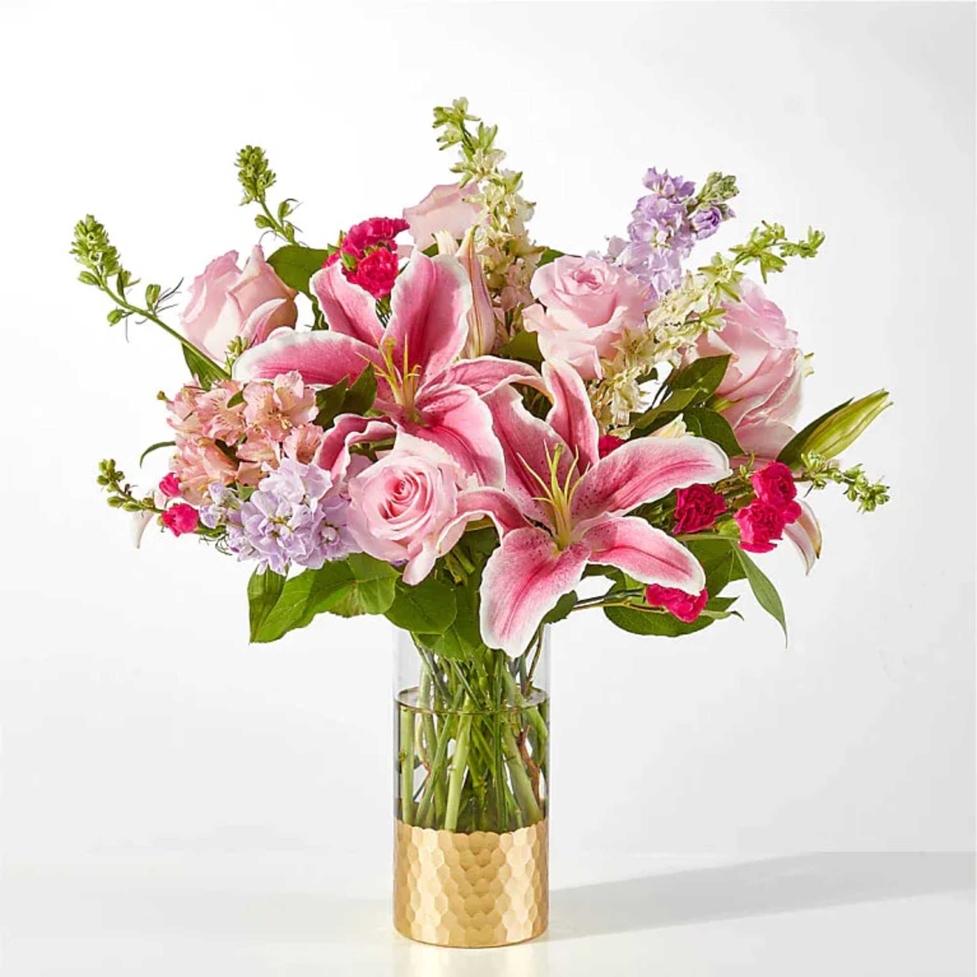 Pink lilies and roses arranged in a glass vase with a gold base