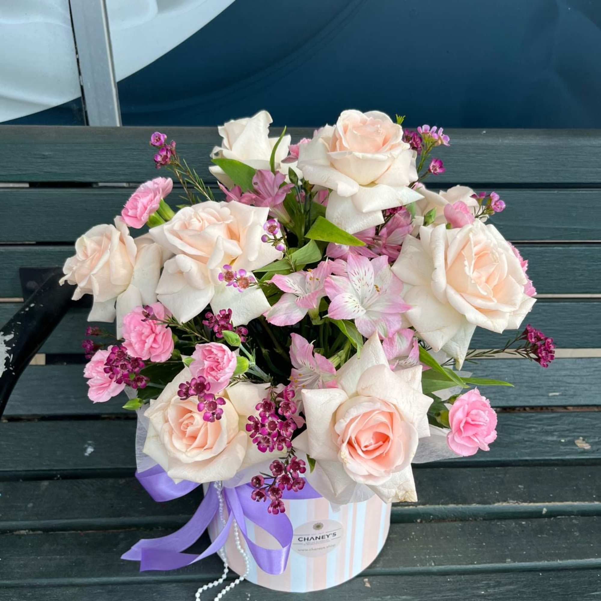 Bouquet of pale pink roses and small pink flowers in a striped box