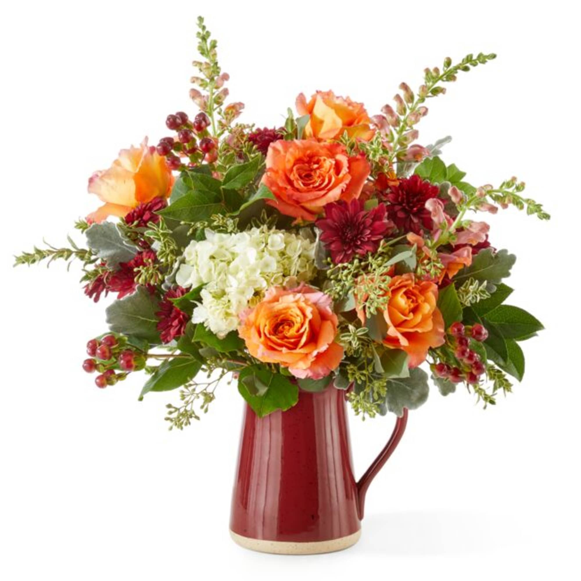 Orange roses and burgundy flowers in a red pitcher vase