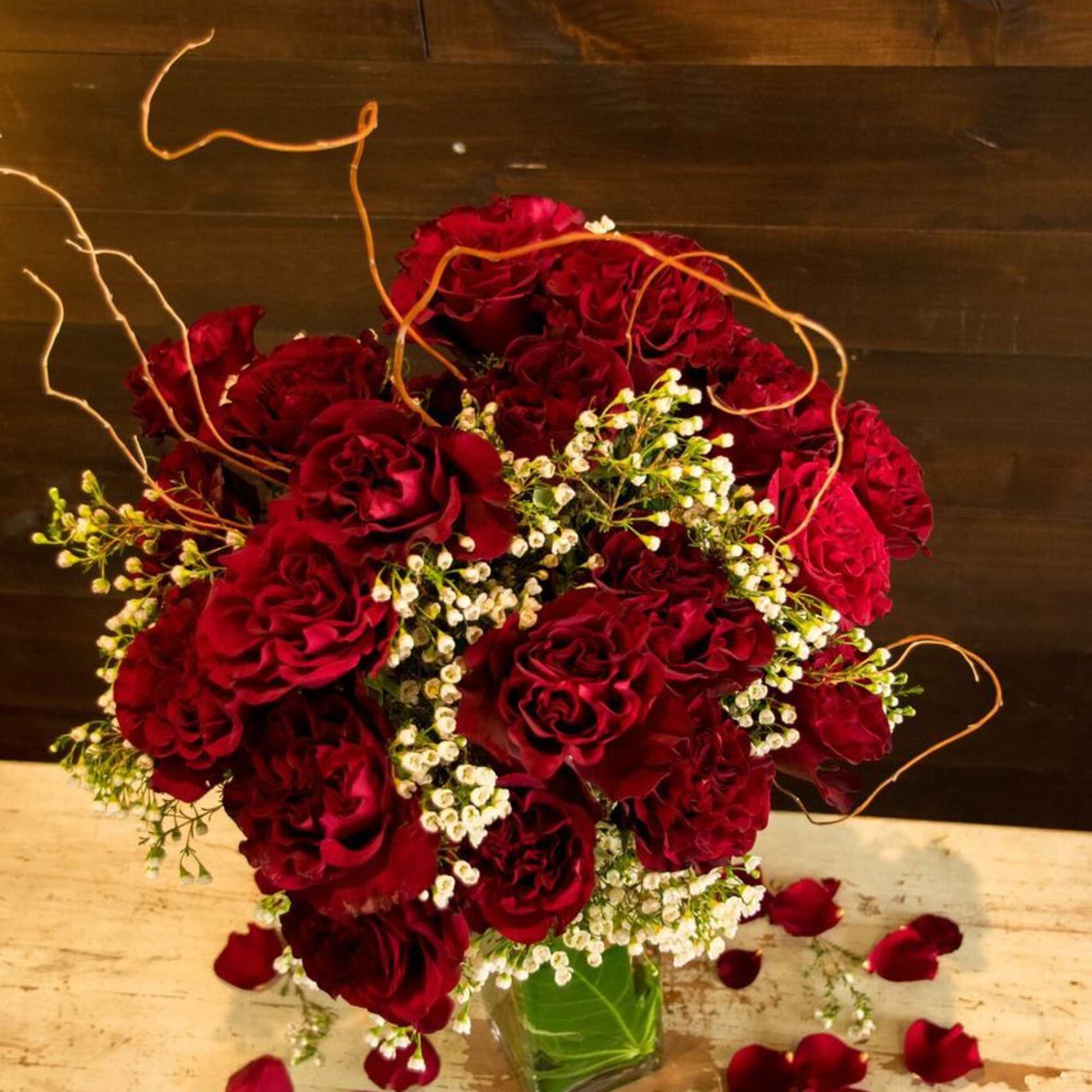 Red rose bouquet in a clear glass vase with scattered petals