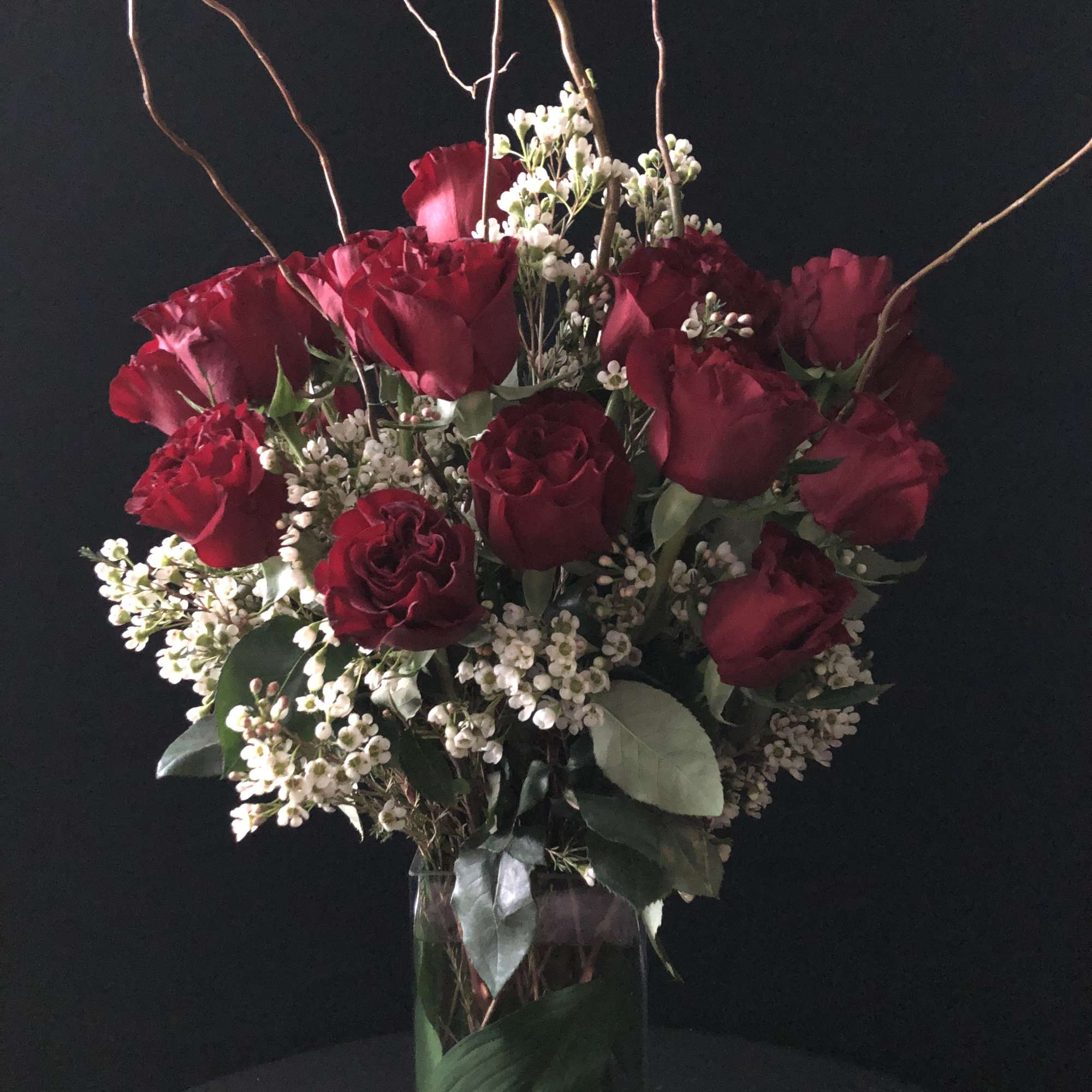 Red roses and white filler flowers in a tall glass vase with curly branches