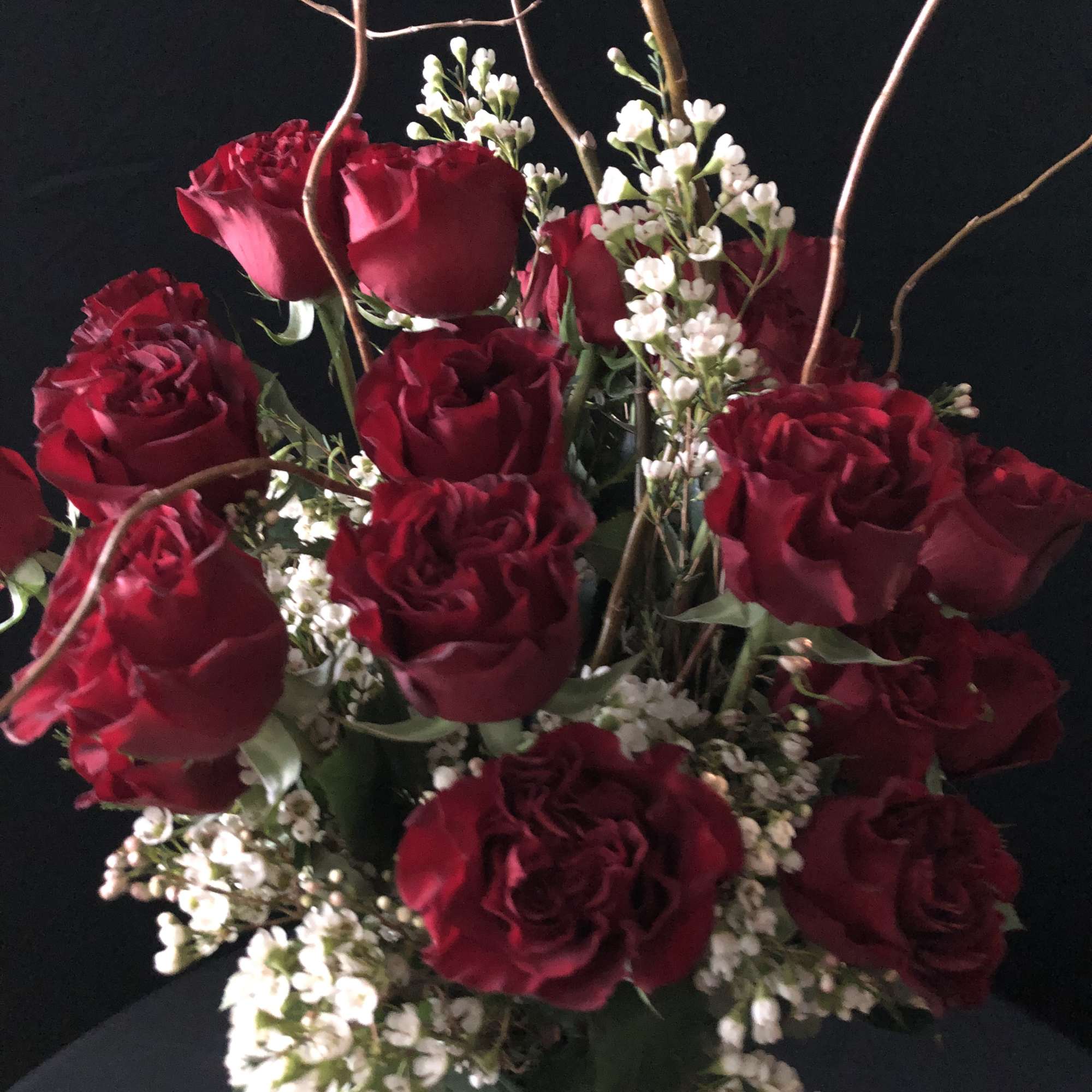 Bouquet of deep red roses with small white filler flowers and curly branches