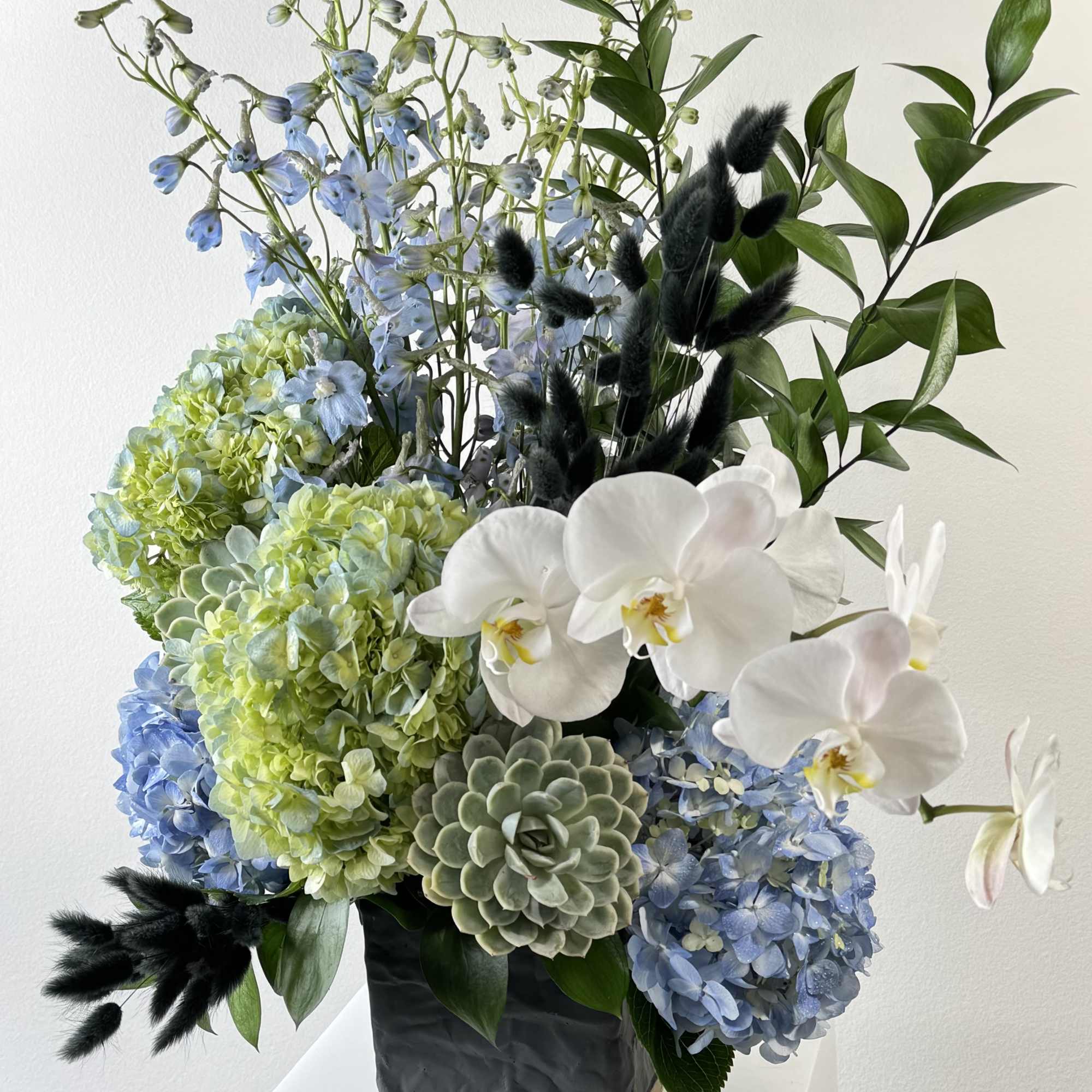 Blue and green floral arrangement with white orchids in a black vase