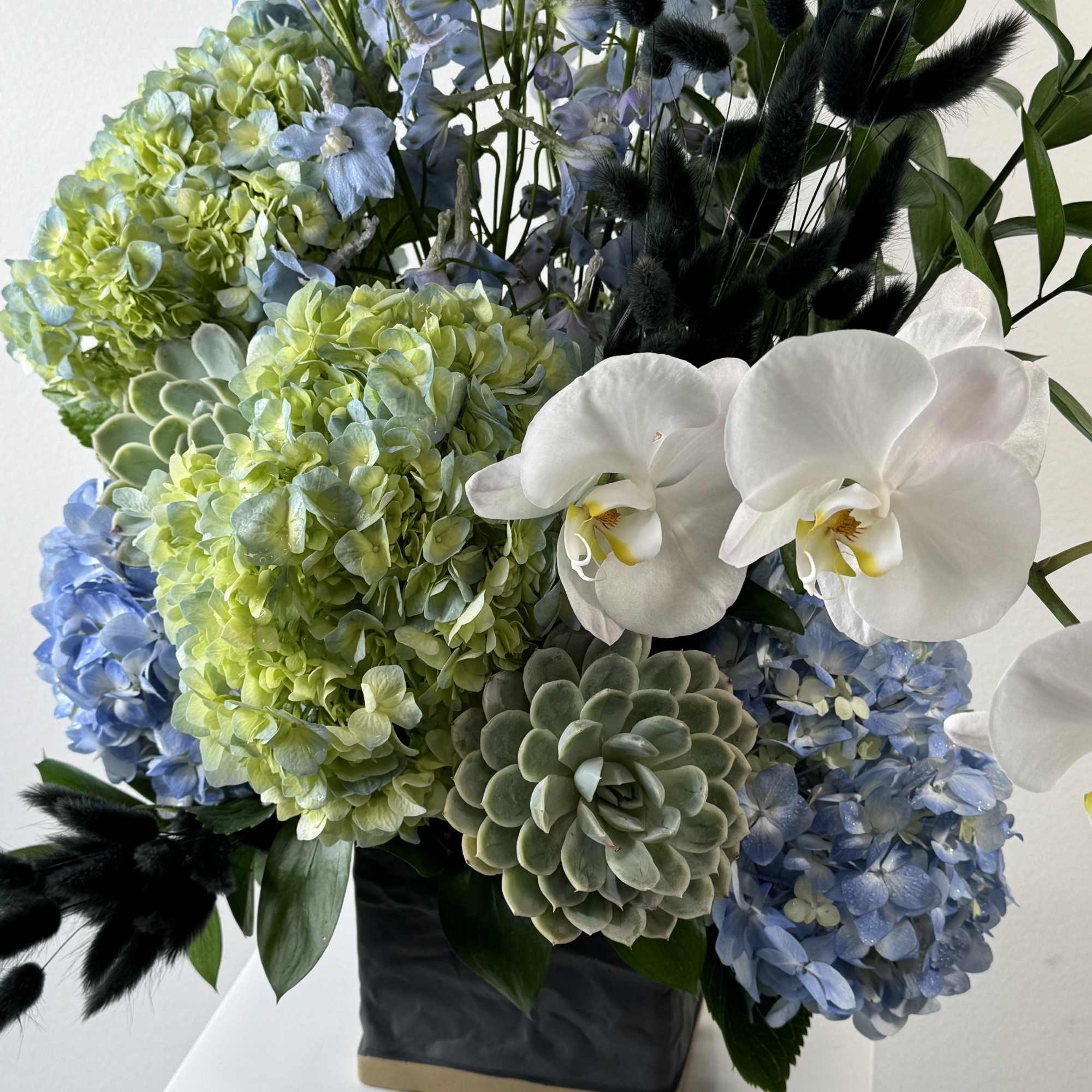 Blue and green floral arrangement with white orchids in a black vase, photo 2 of 2