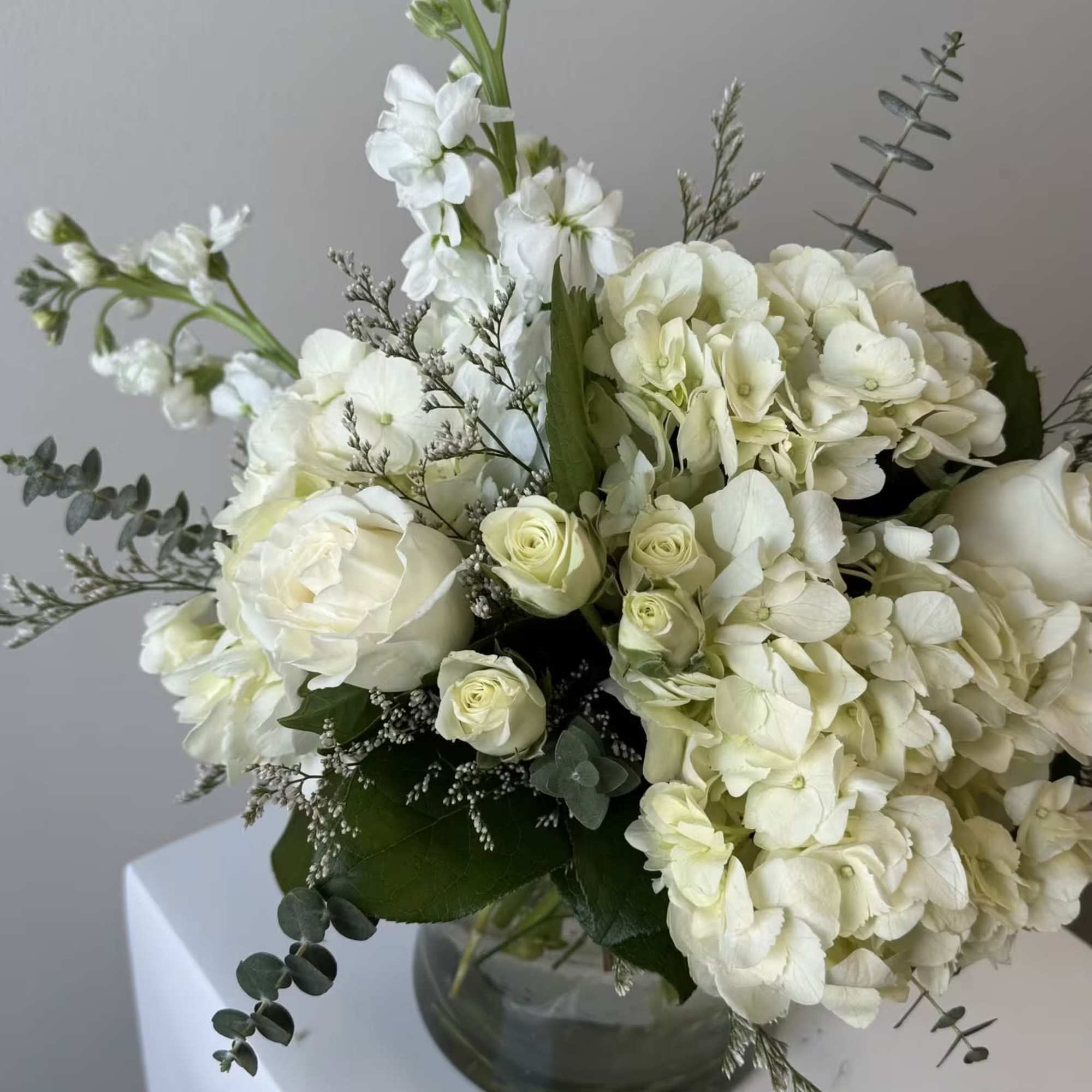 White floral arrangement in a glass vase with roses and hydrangeas