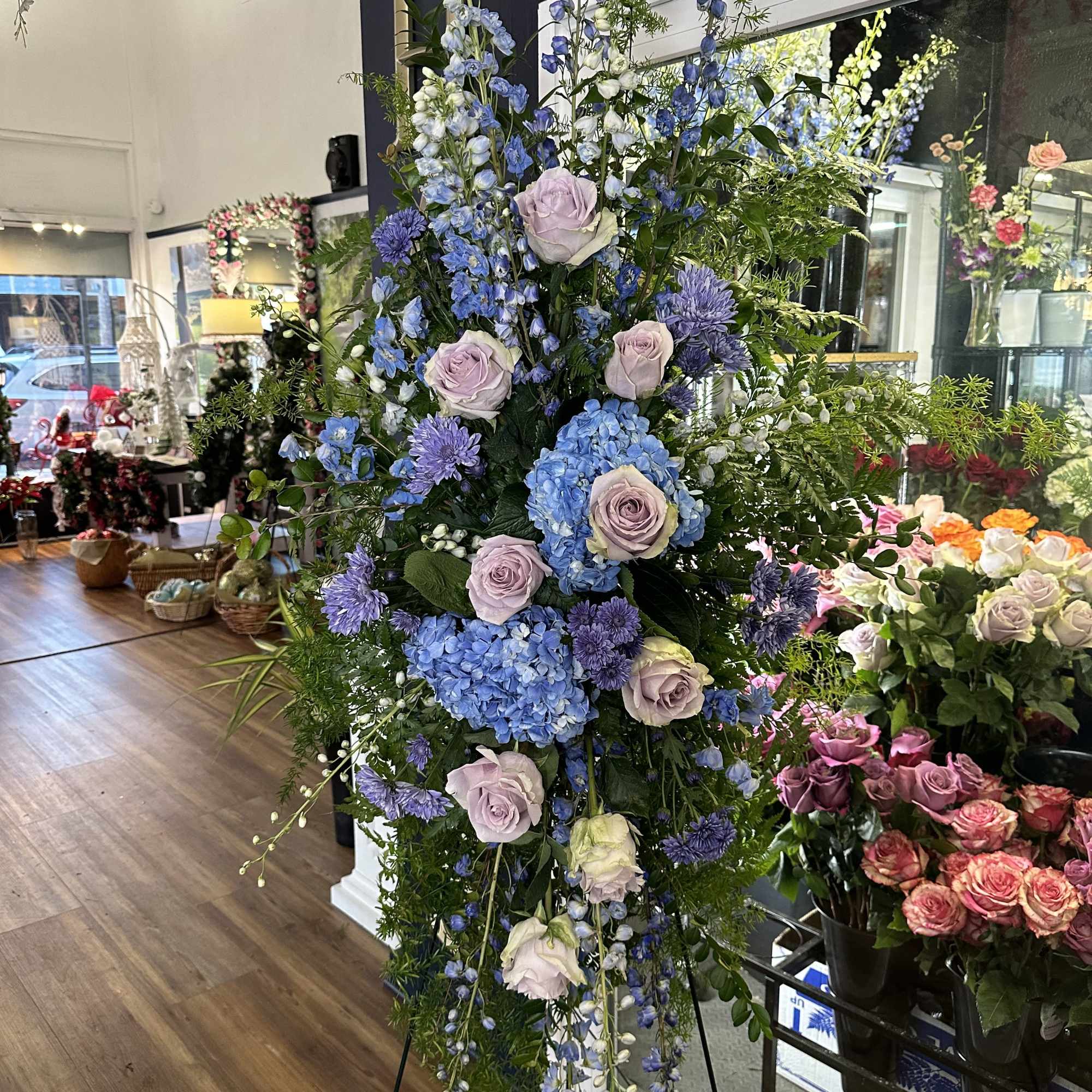 Tall floral standing spray with blue hydrangeas, lavender roses, and purple blooms