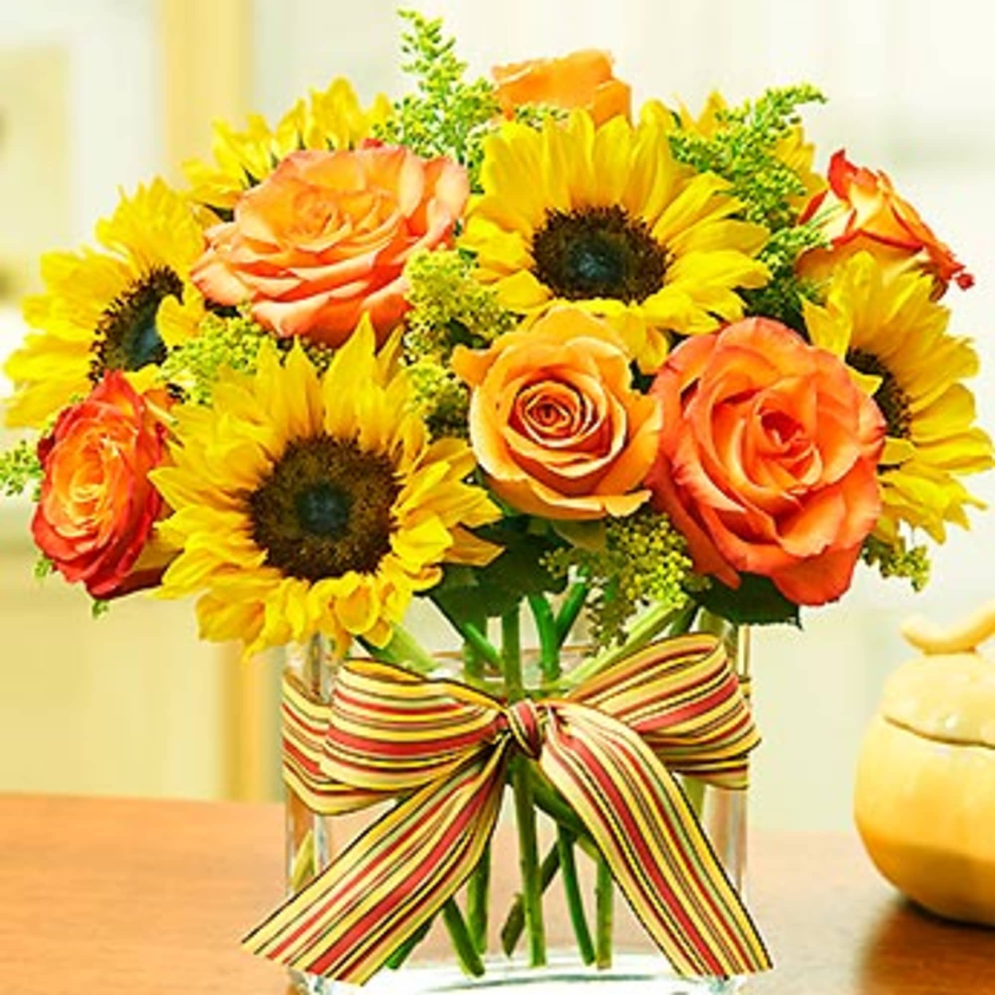 Sunflowers and orange roses in a glass vase with a striped ribbon