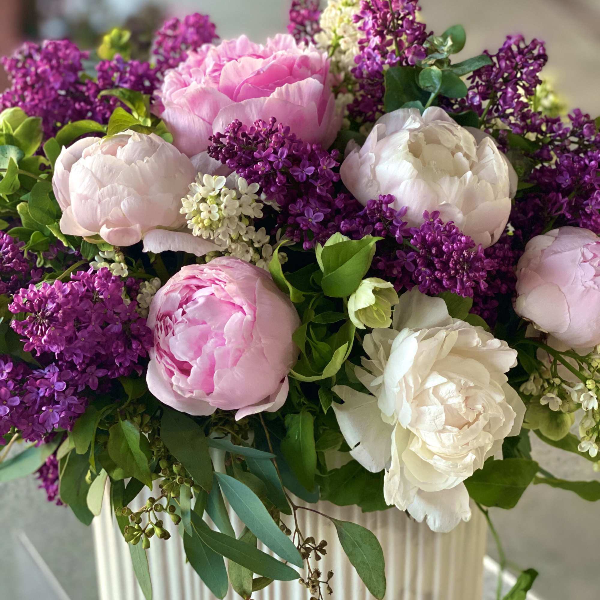 Pink and white peonies with purple lilac in a striped vase