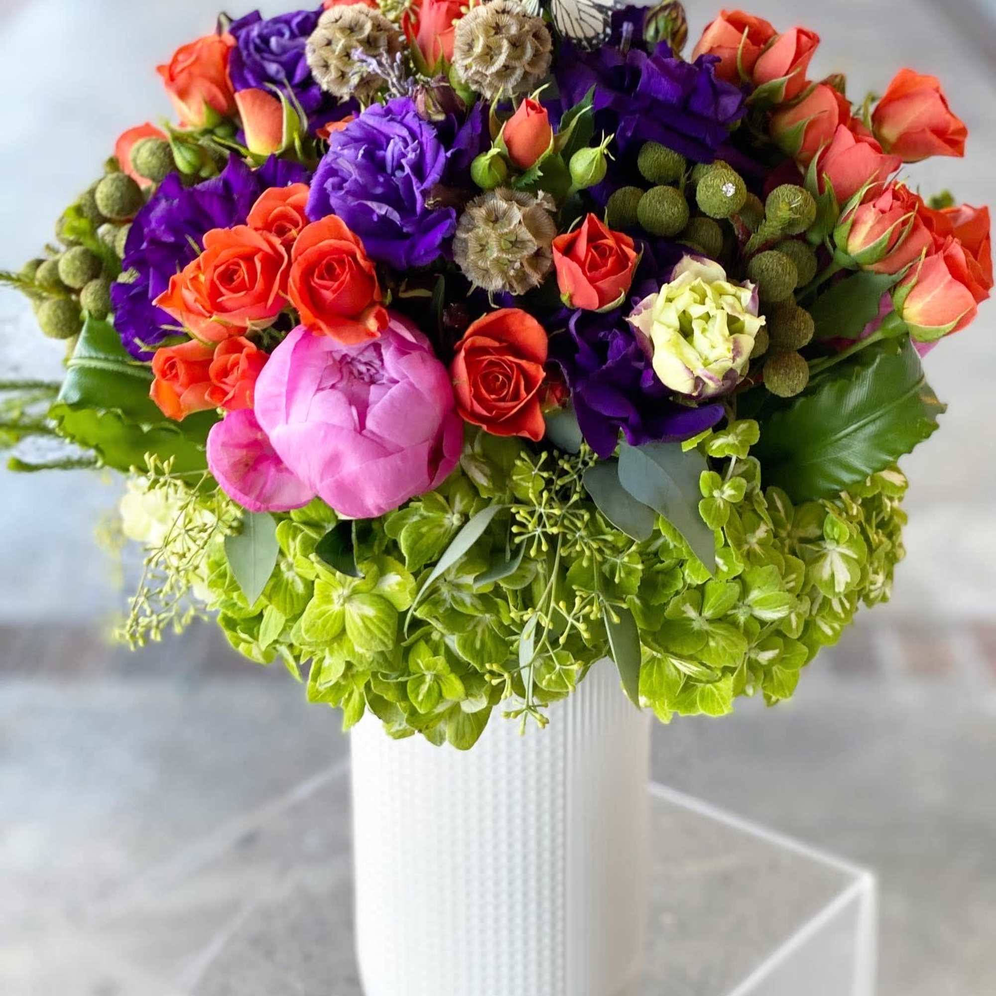 Colorful bouquet of roses and purple blooms in a white vase