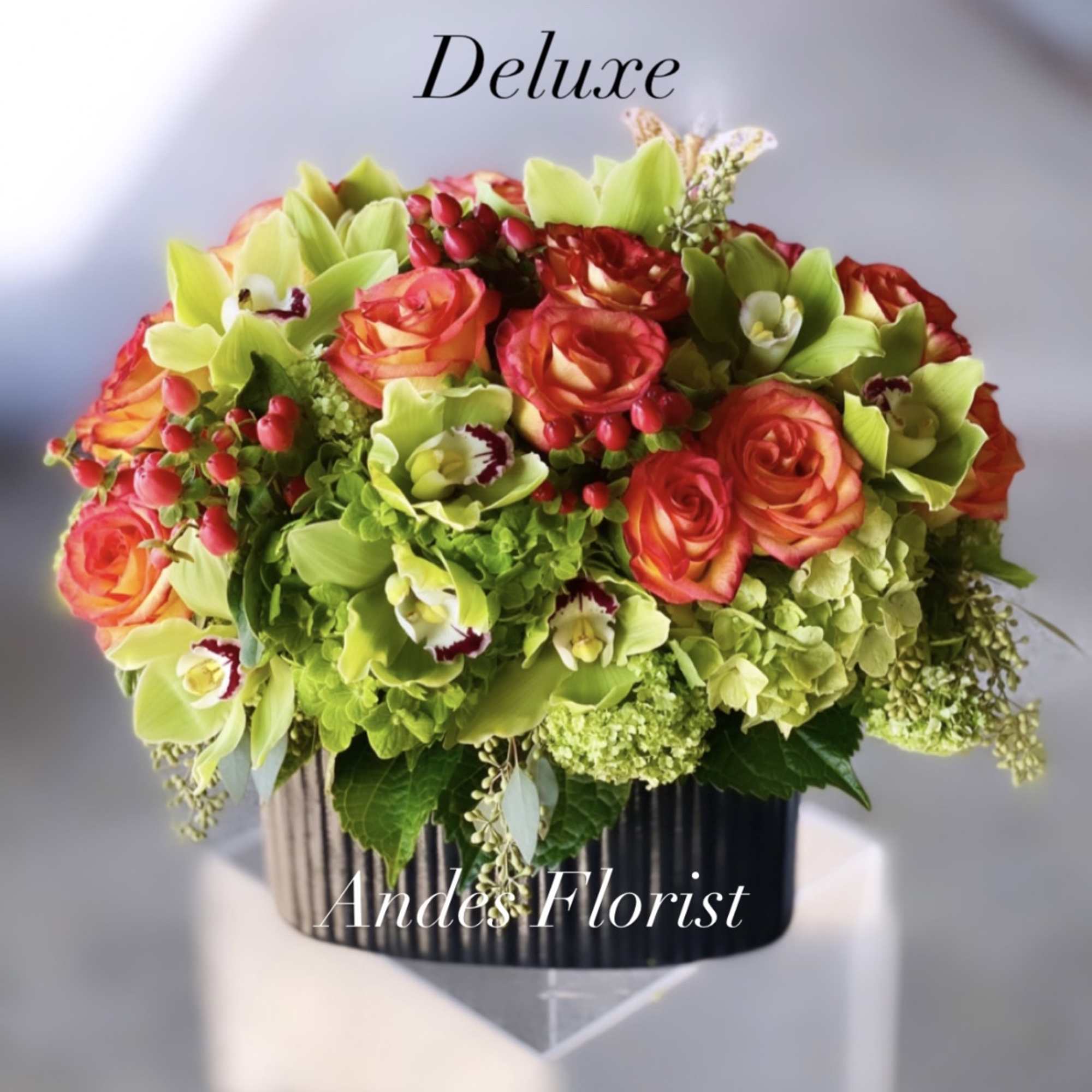 Bouquet of orange roses and green orchids in a black vase
