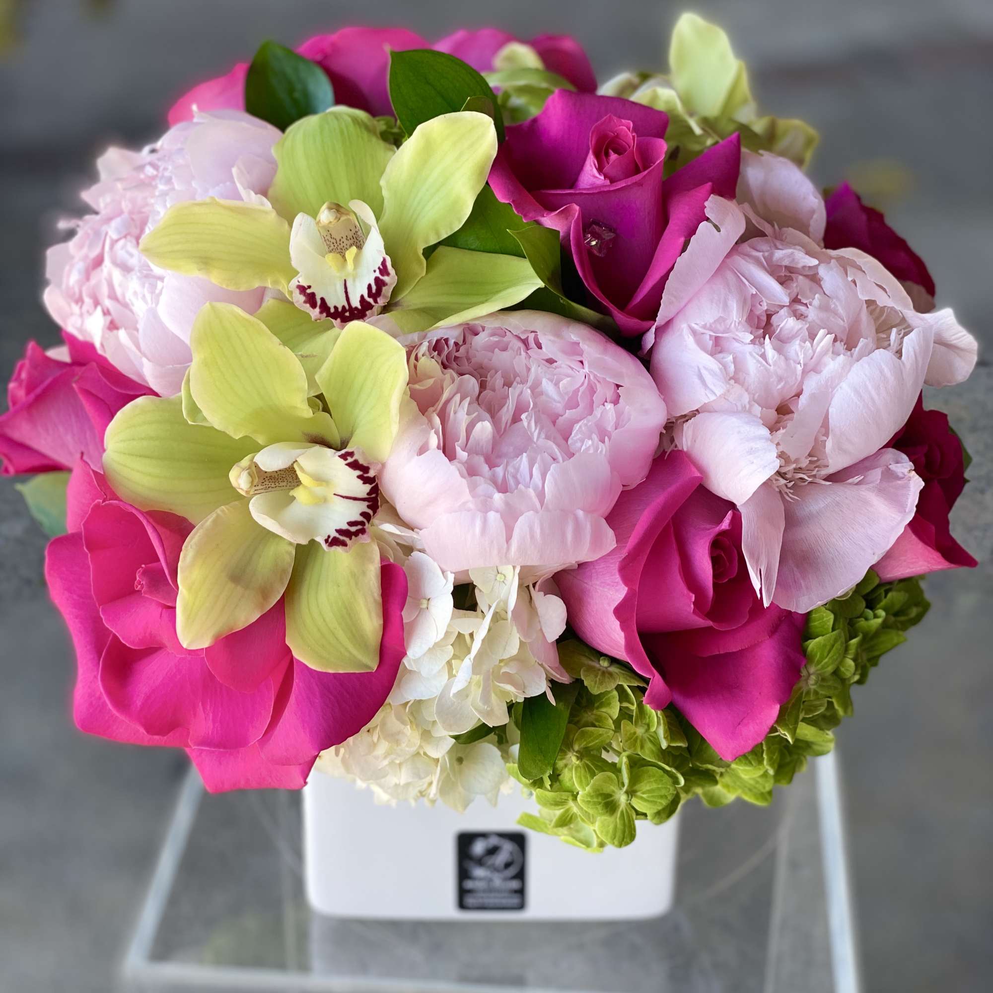 Pink roses and peonies with green orchids in a white vase