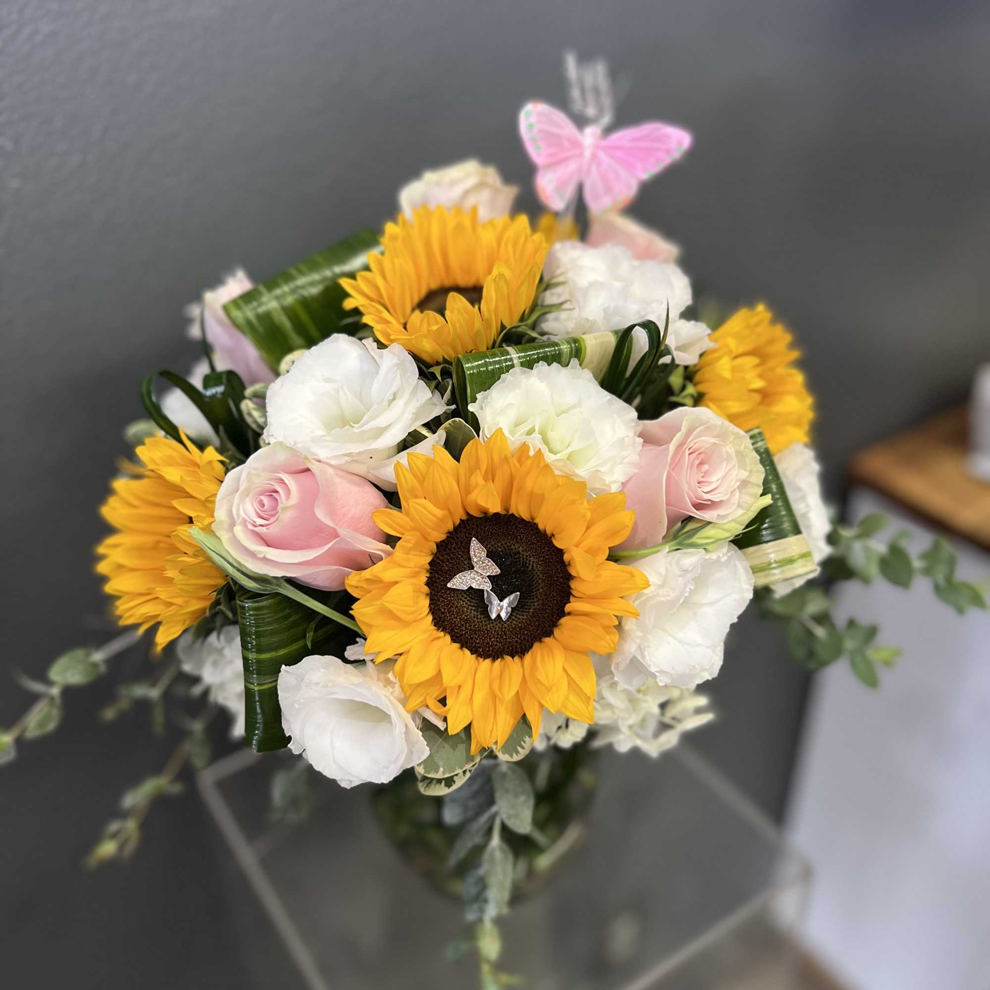 Bouquet of sunflowers, pink roses, and white blooms with a butterfly pick