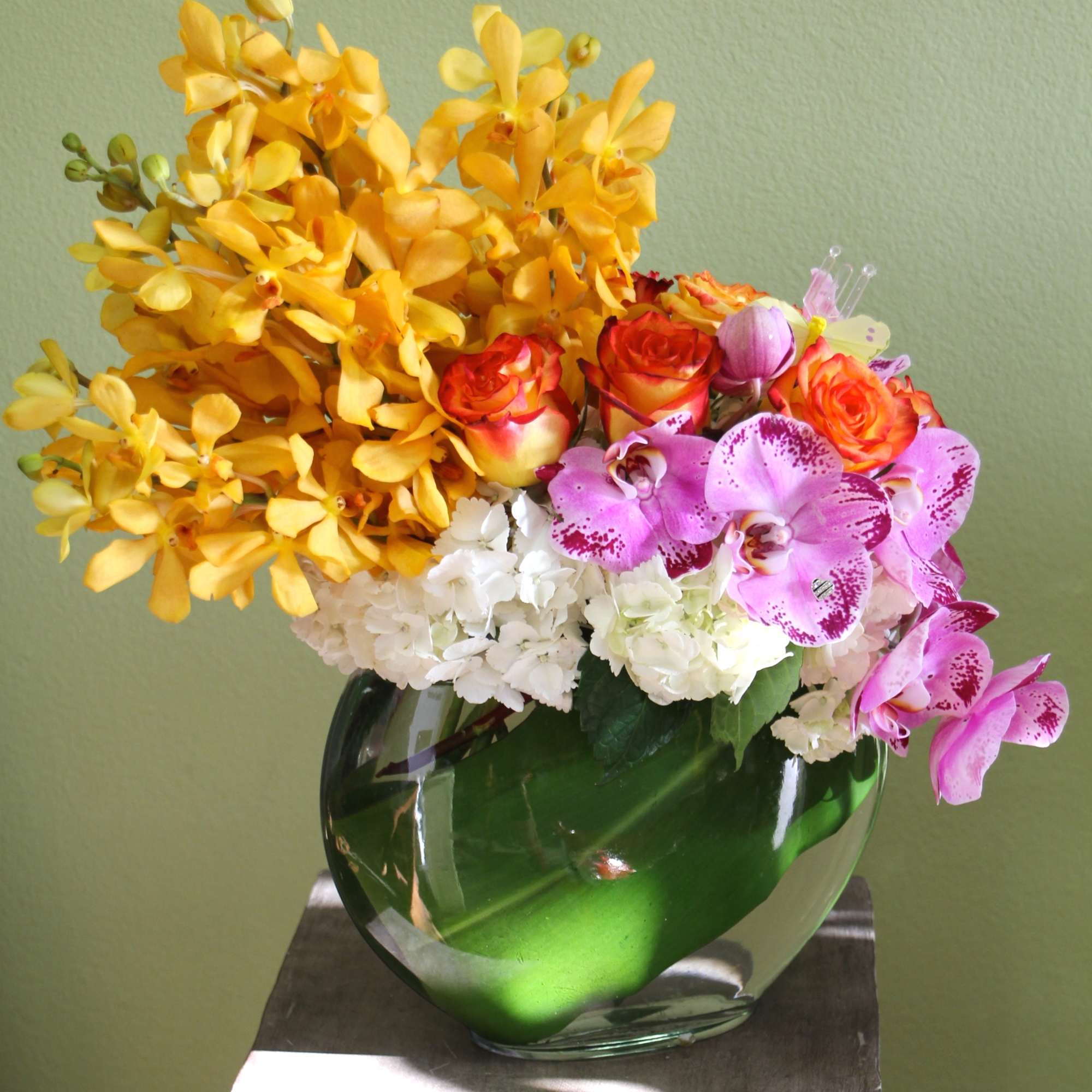 Yellow orchids, pink orchids, roses, and white hydrangeas in a glass vase