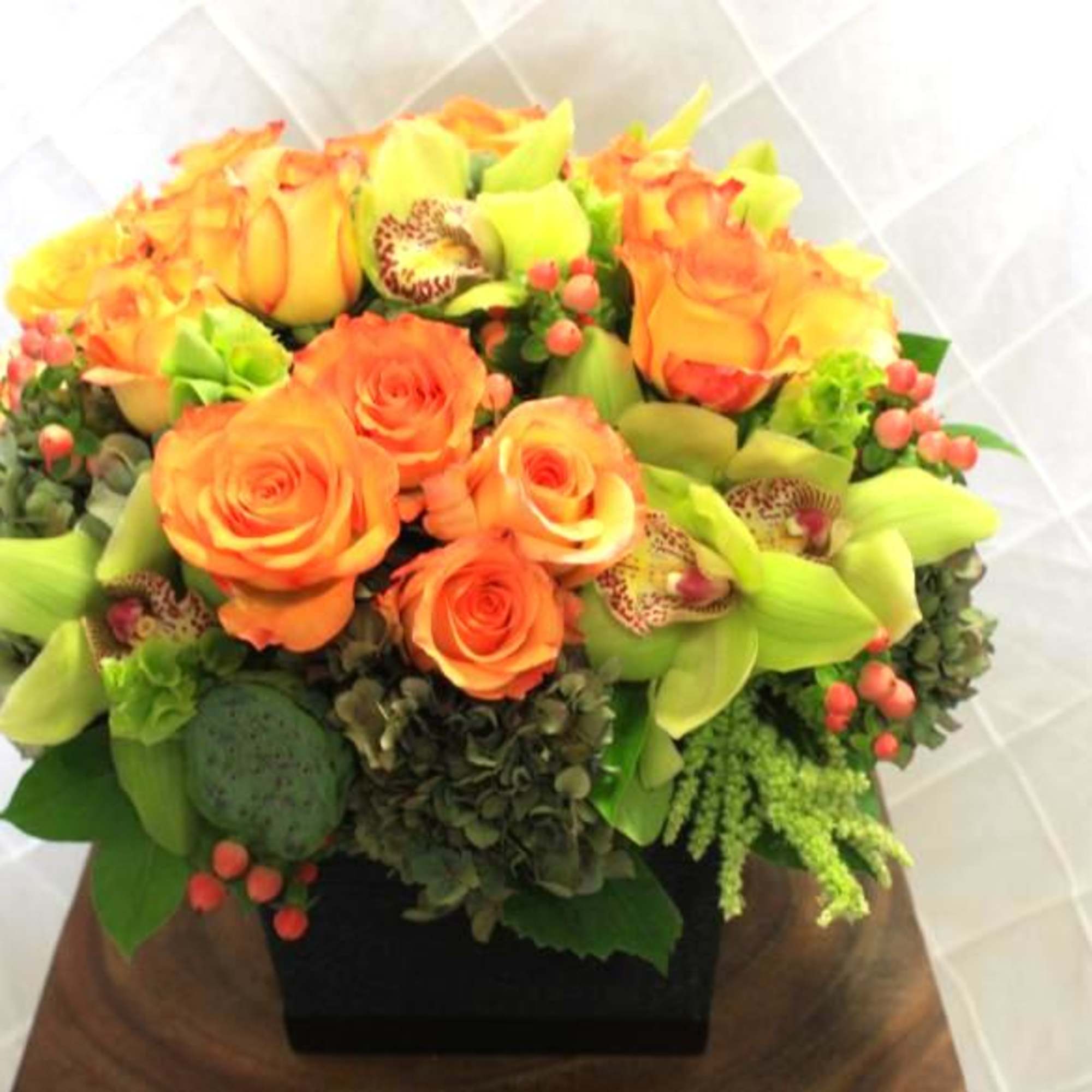 Orange roses and green orchids in a black square vase