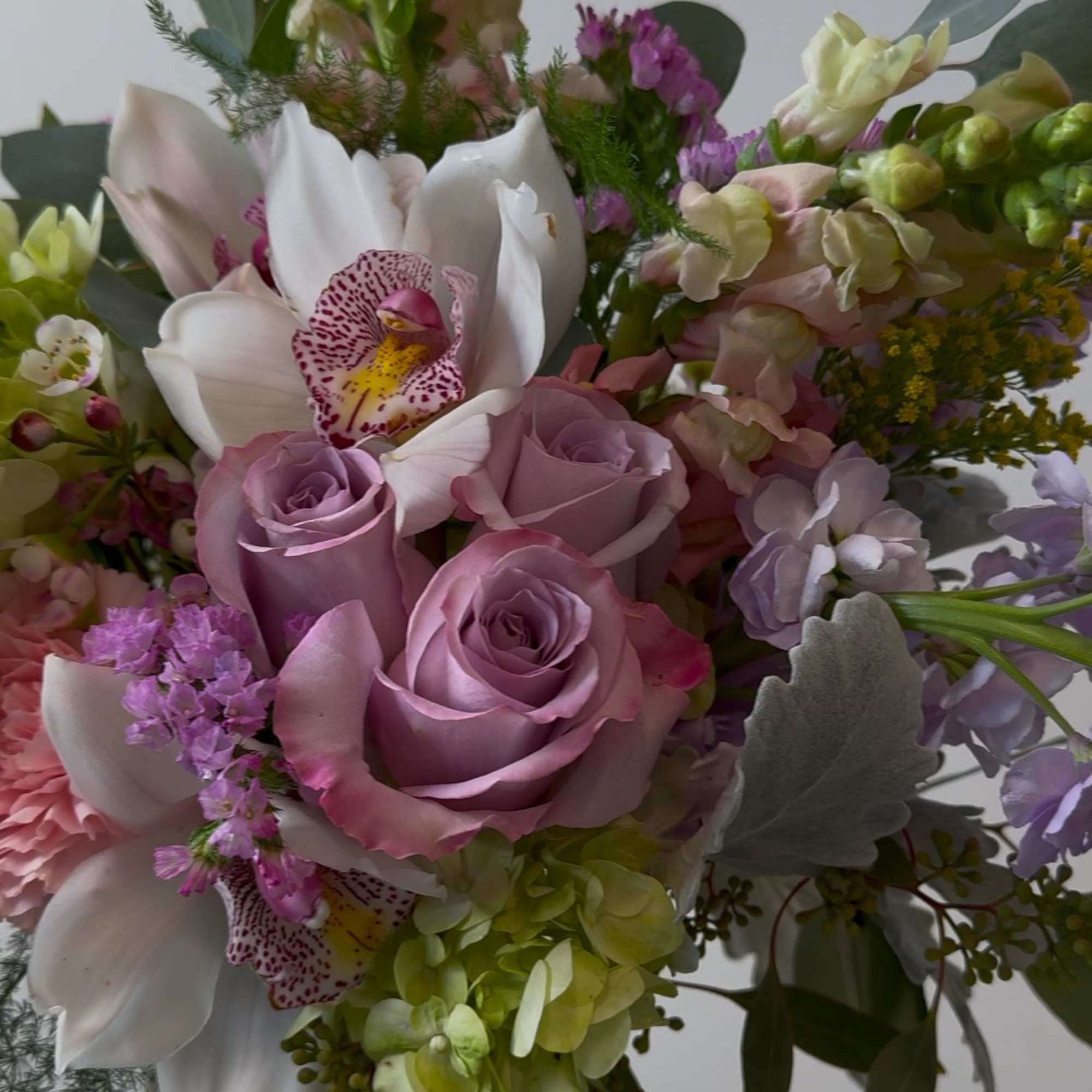 Mixed bouquet of pink roses, white orchids, and pastel blooms in a glass vase