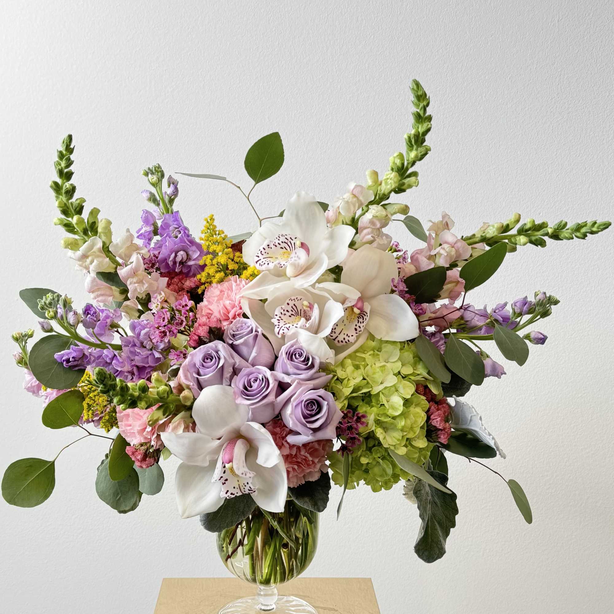 Mixed bouquet of lavender roses, white orchids, and pink blooms in a glass vase
