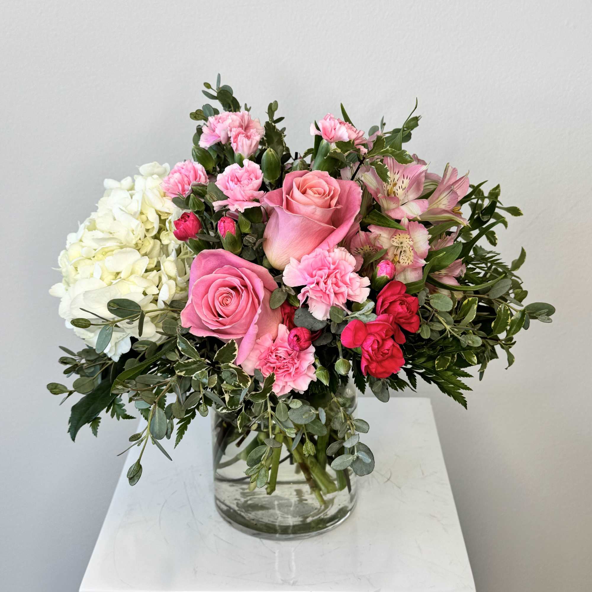 Pink roses, carnations, and white hydrangeas arranged in a clear glass vase