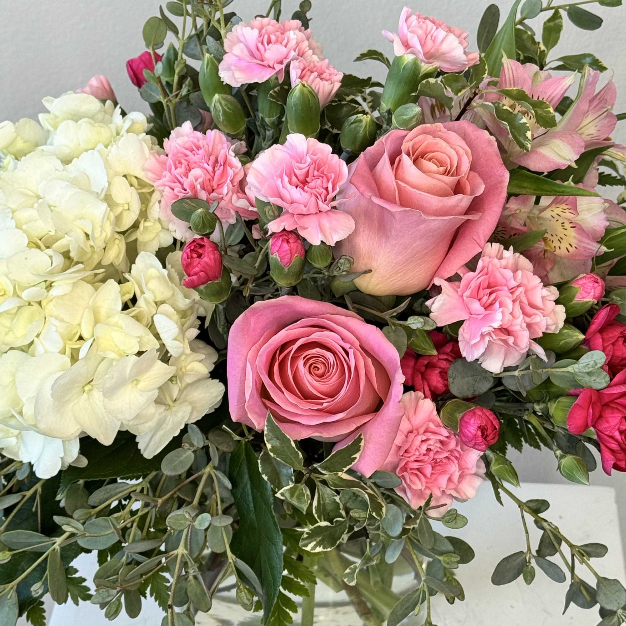 Low glass vase of pink roses, pink carnations, and white hydrangeas in a compact arrangement