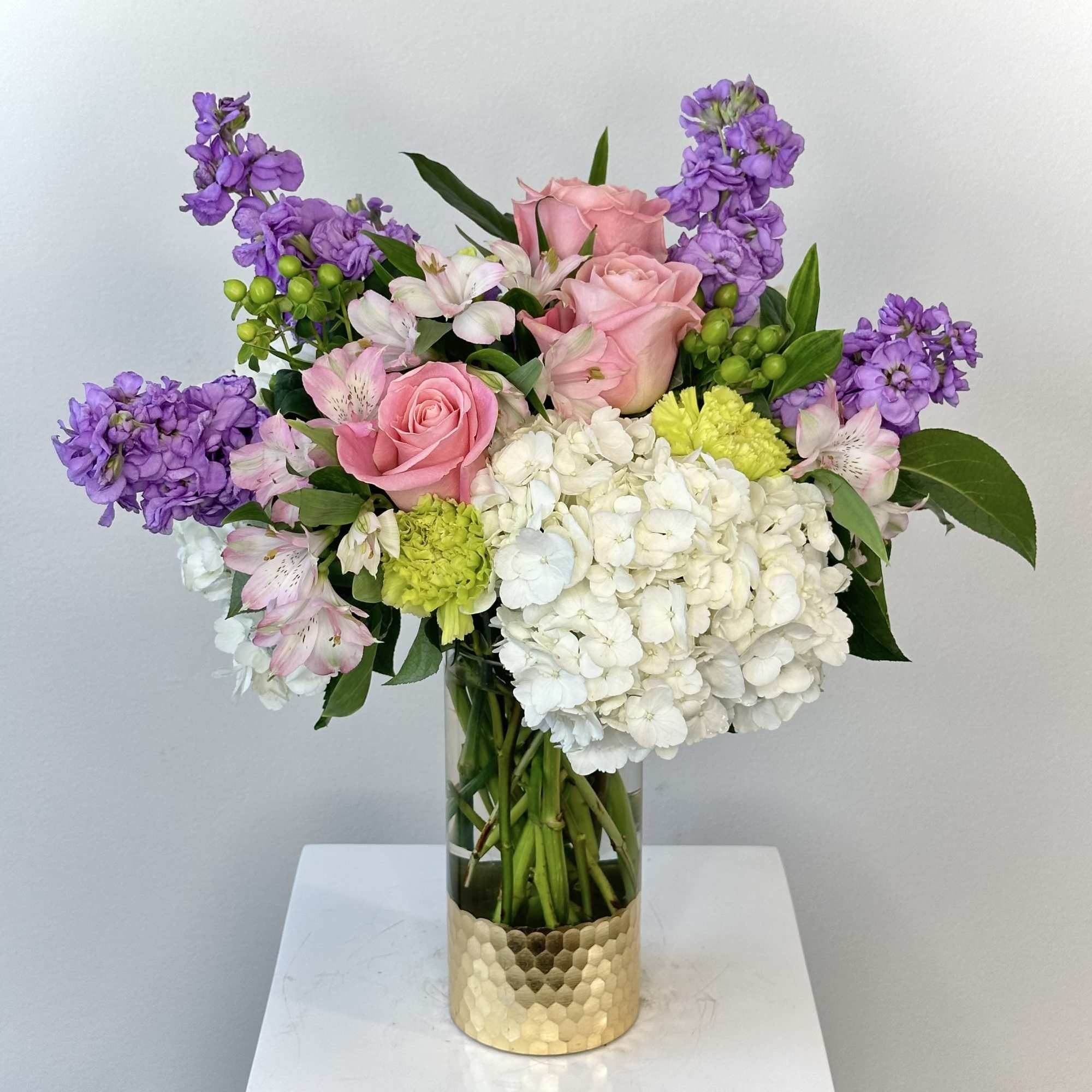Pink roses, white hydrangea, and purple flowers in a gold vase